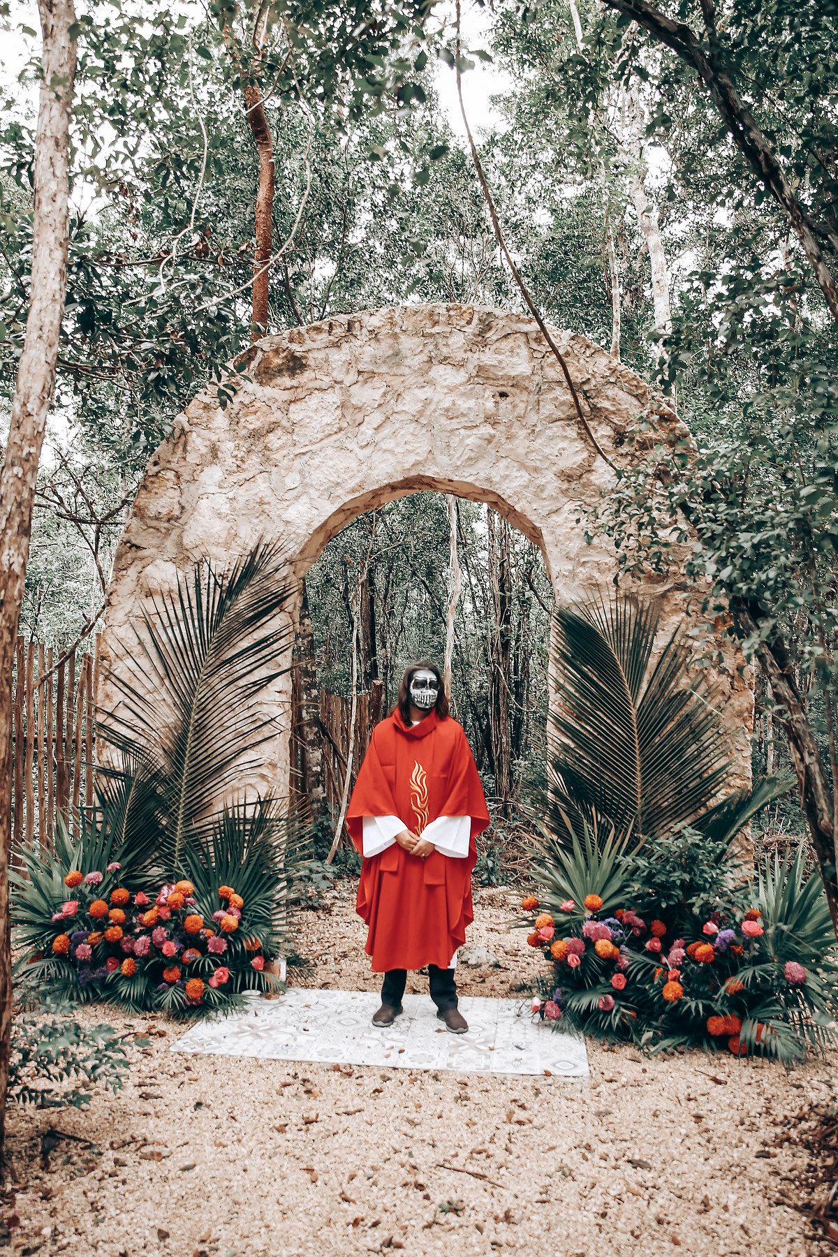 Stone archways in a wooded garden setting decorated with vibrant red roses and palm fronds create a romantic atmosphere.