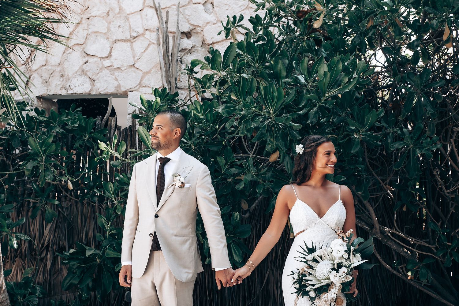 Wedding party posing outdoors against lush greenery in formal attire.