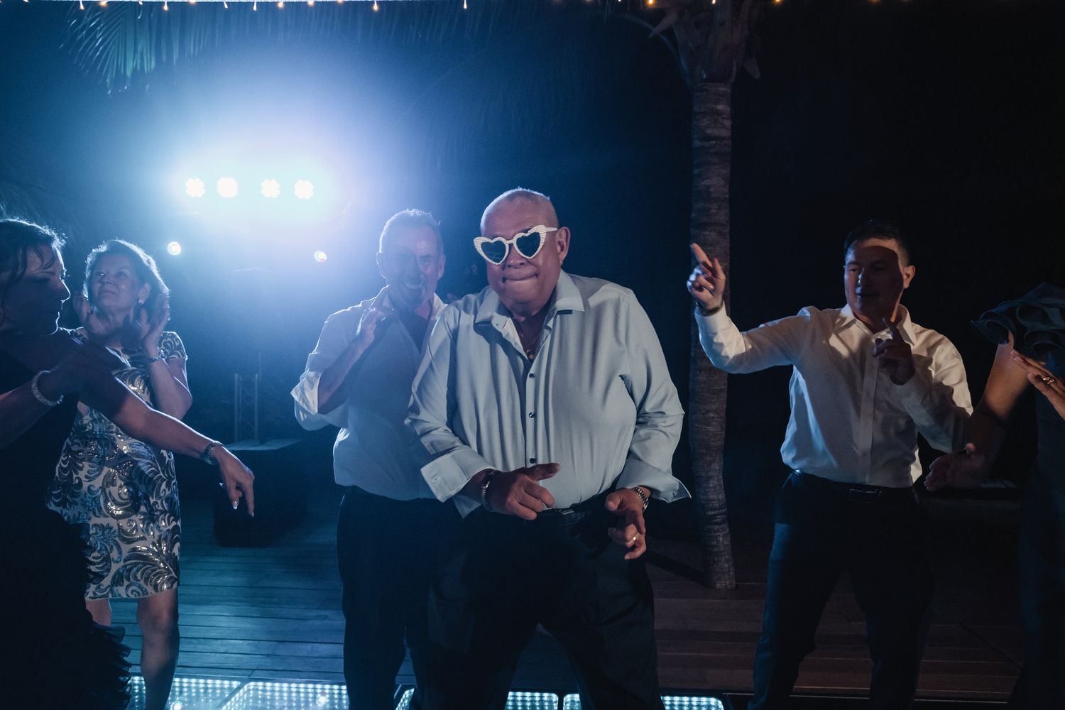 Elderly guest wearing oversized sunglasses dancing at outdoor wedding reception at night.