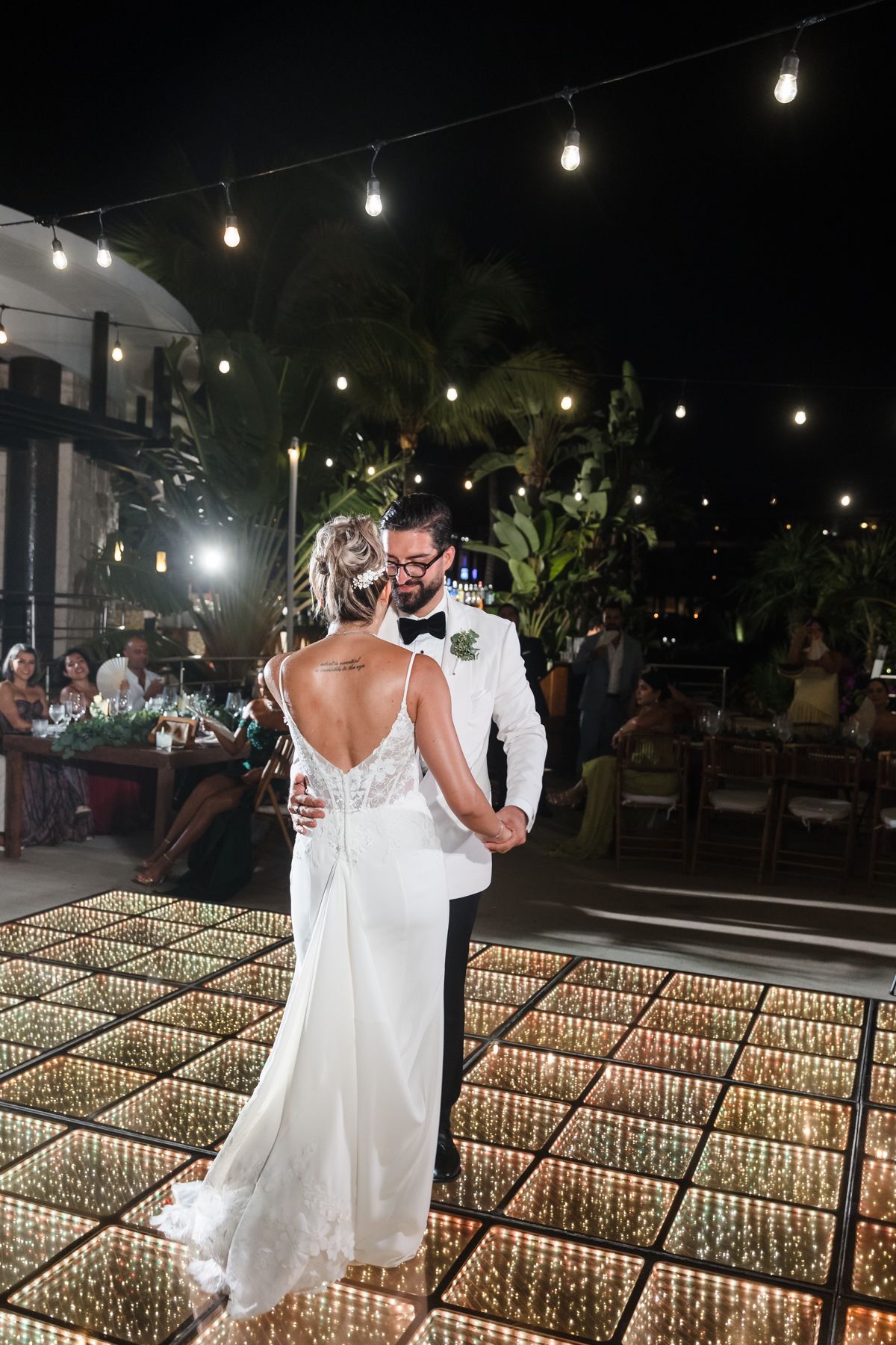 Bride and groom share their first dance on a glowing LED dance floor at an elegant outdoor wedding reception at night.
