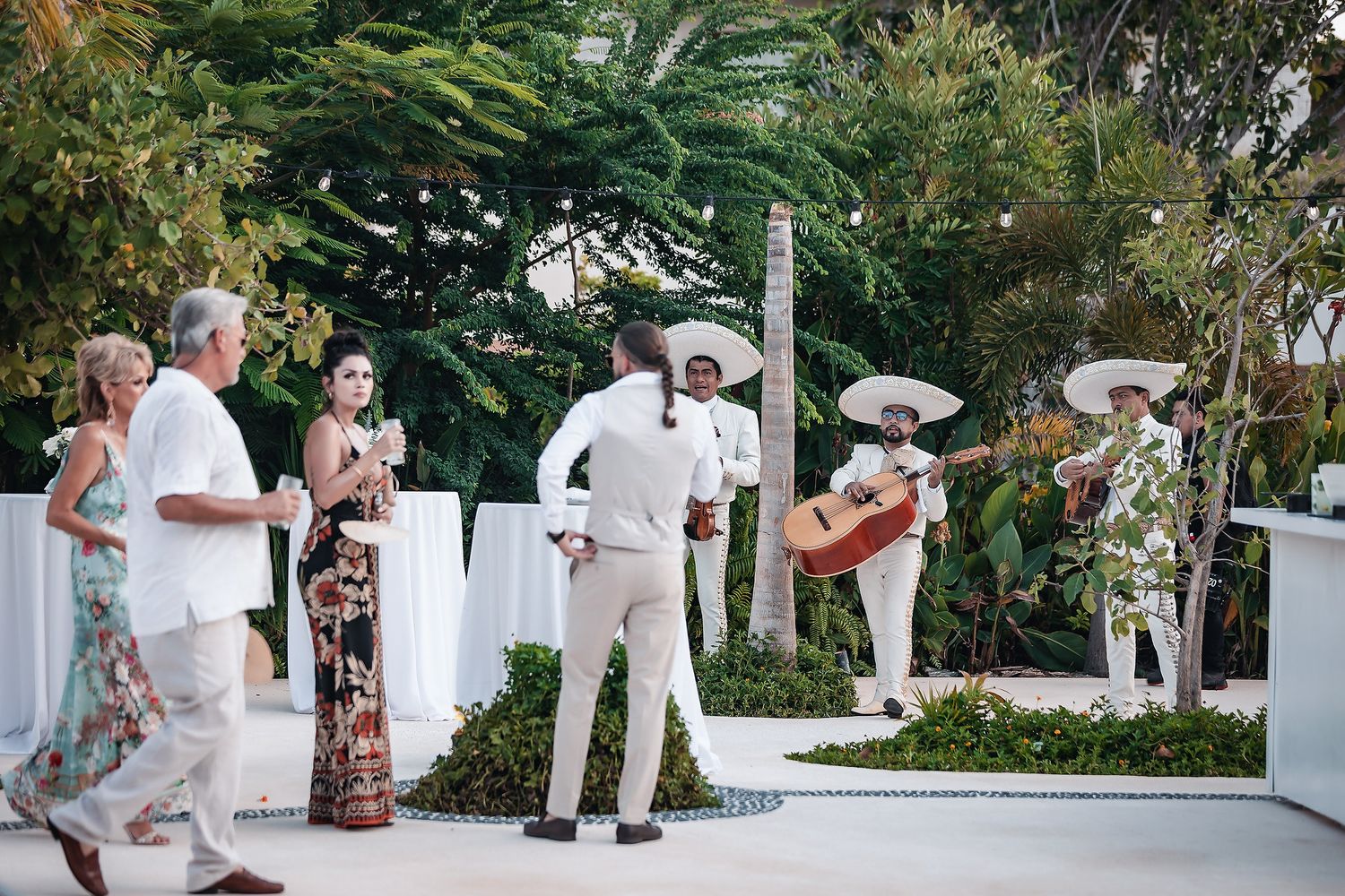 Mariachi band performs for guests at an outdoor destination wedding reception surrounded by tropical greenery.