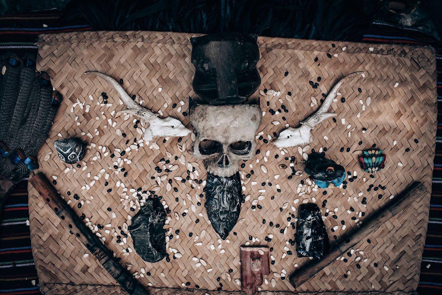 A decorative woven mat displays a skull with horns, surrounded by small objects and scattered beads.