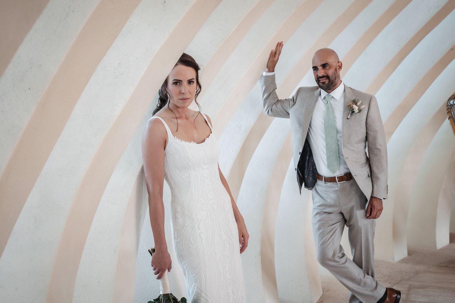 Bride in white dress and groom in gray suit walking together at an outdoor wedding venue.