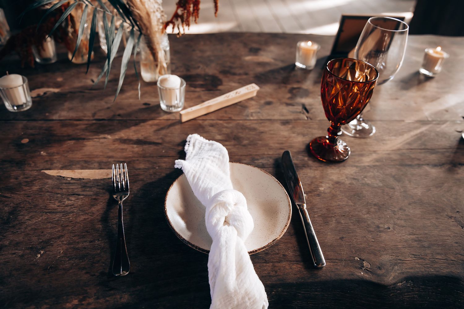 A rustic wooden table setting with white napkins, wine glasses, and plates in a dimly lit restaurant interior.