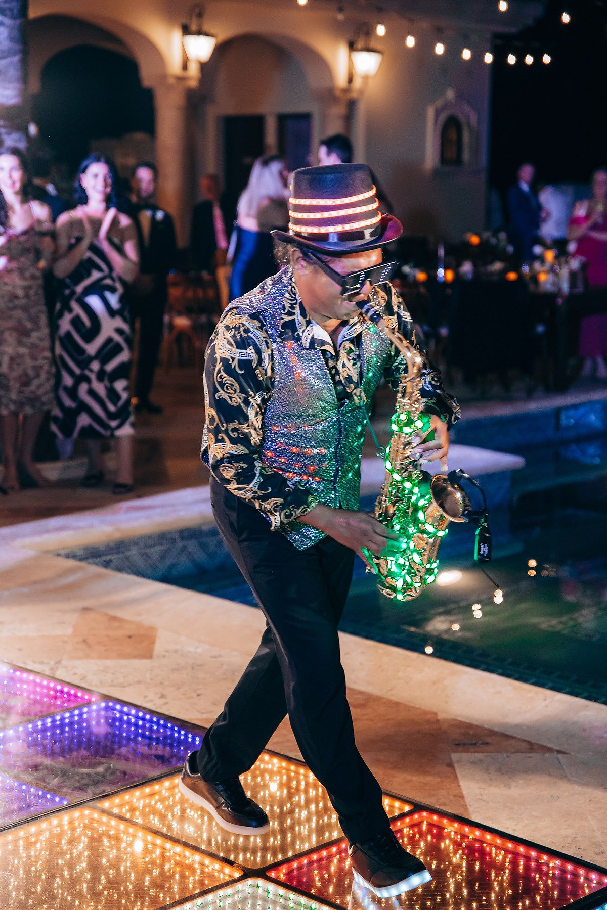 Dancers perform on a colorful illuminated dance floor with LED lights and sparkles at a nighttime party.