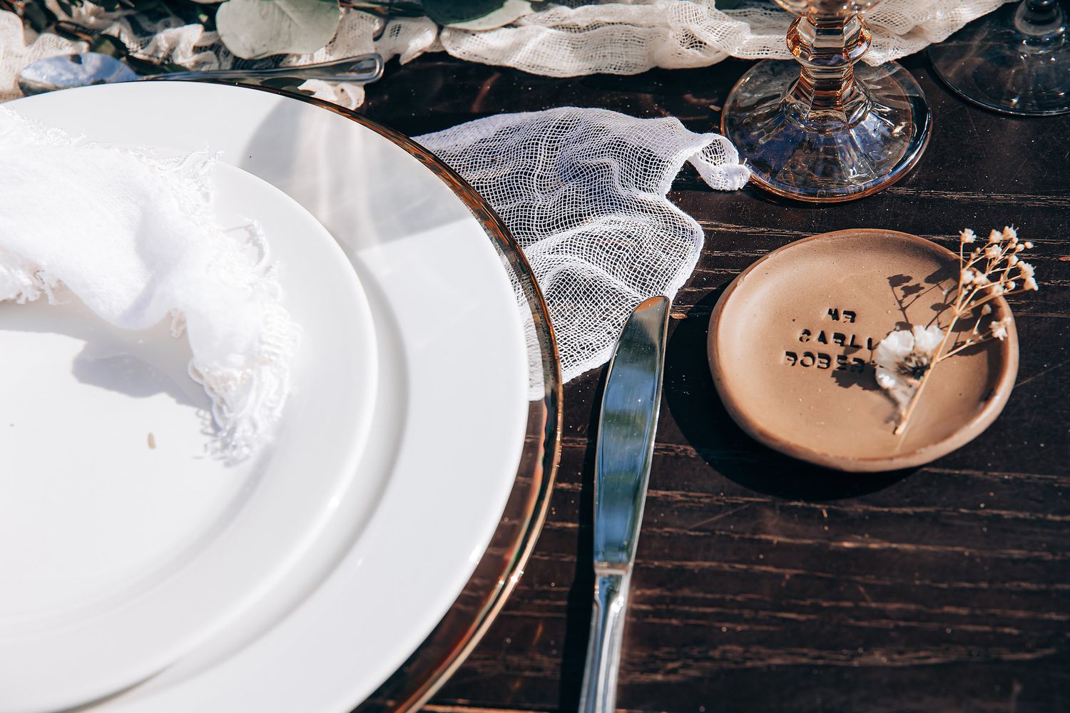 Elegant place settings with white plates and delicate floral accents on a dark wooden table at a formal dinner.