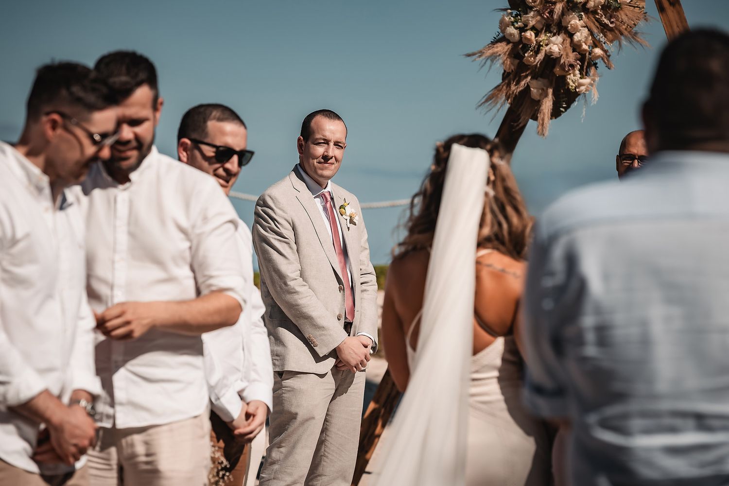 Guests gather under palm trees at a beachside wedding celebration.