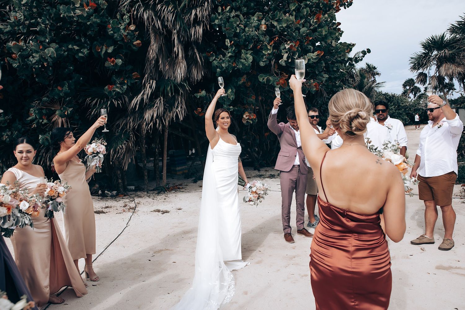 Wedding celebration on a sandy beach with guests in burgundy and neutral colored attire.