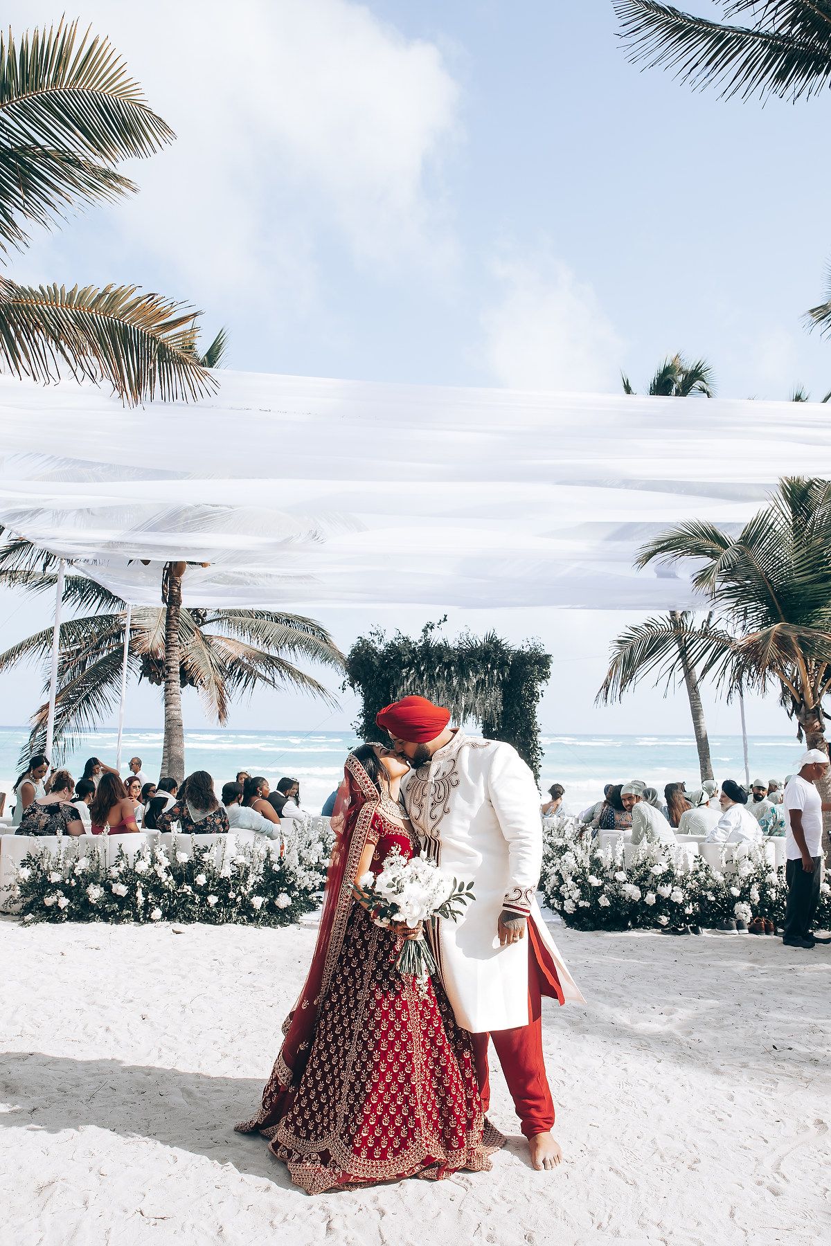 Destination Indian wedding ceremony on a white sandy beach with palm trees.