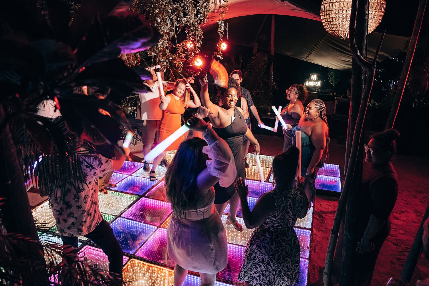 Nighttime party scene with red ambient lighting and LED floor creating a vibrant dance atmosphere.