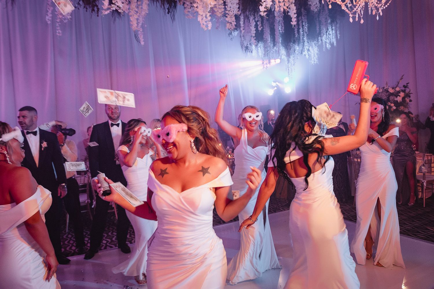 Wedding reception guests dance and celebrate on a purple-lit dance floor during an energetic party celebration.
