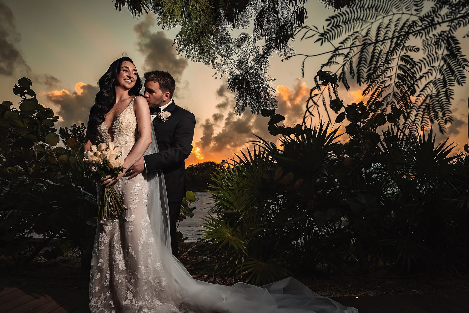Sunset wedding photography session with silhouetted palm trees and warm glowing sky in a tropical setting.