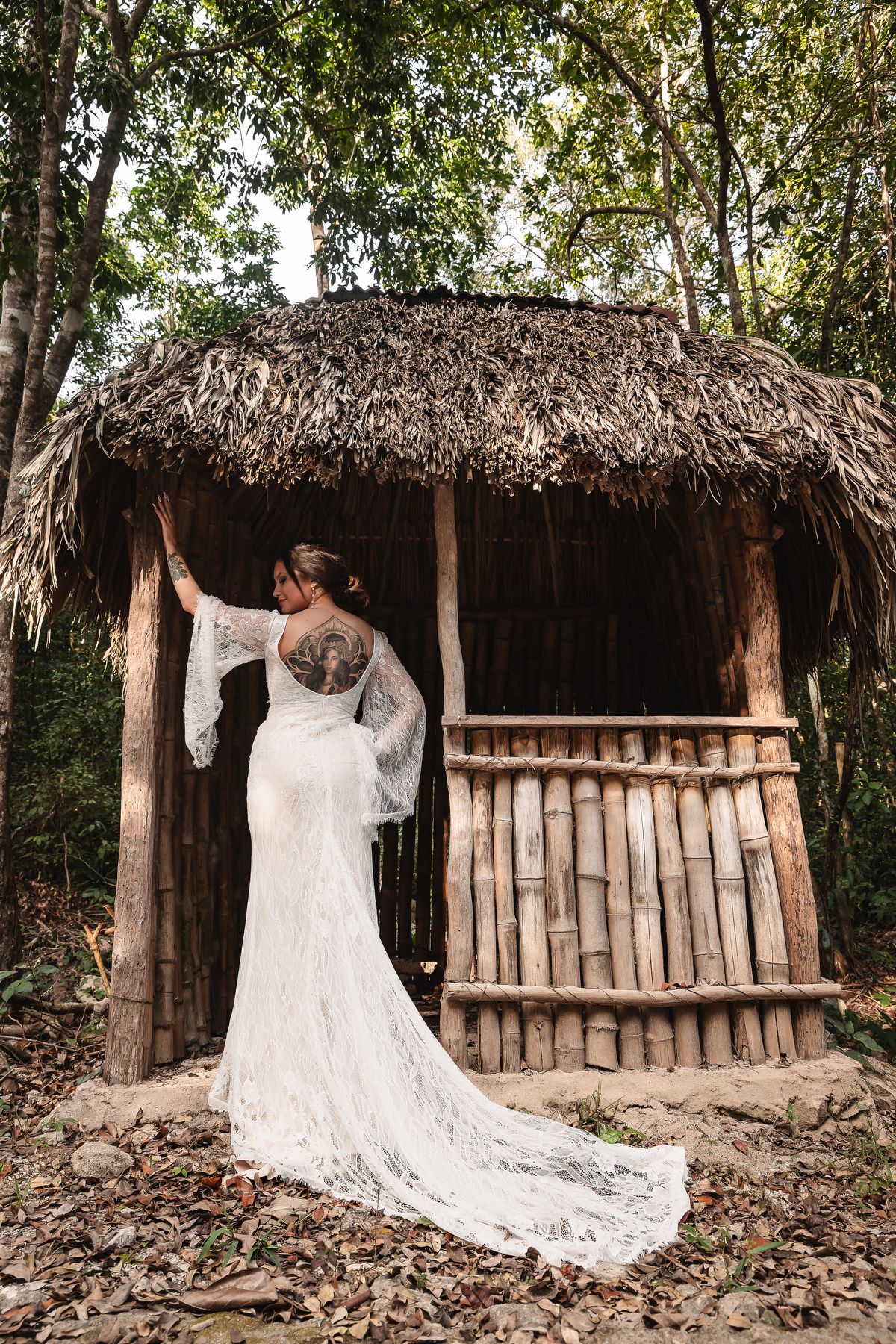 Beautiful white wedding dress with long train displayed against rustic thatched-roof huts in a tropical setting.
