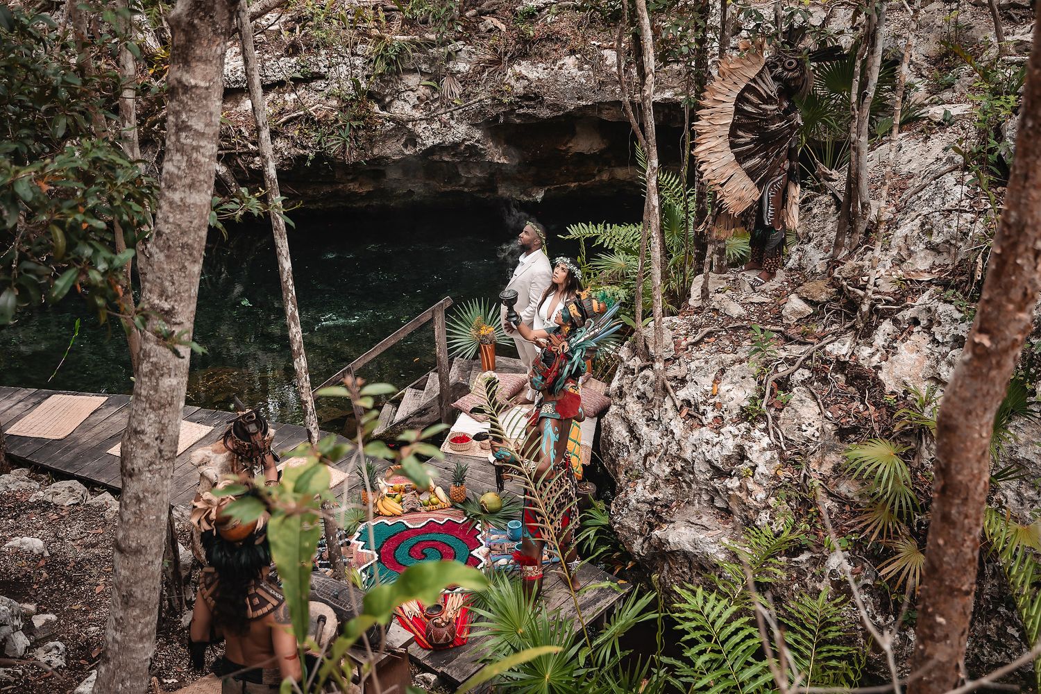 A scenic view of a cenote ceremony setup with colorful blankets and tropical plants.