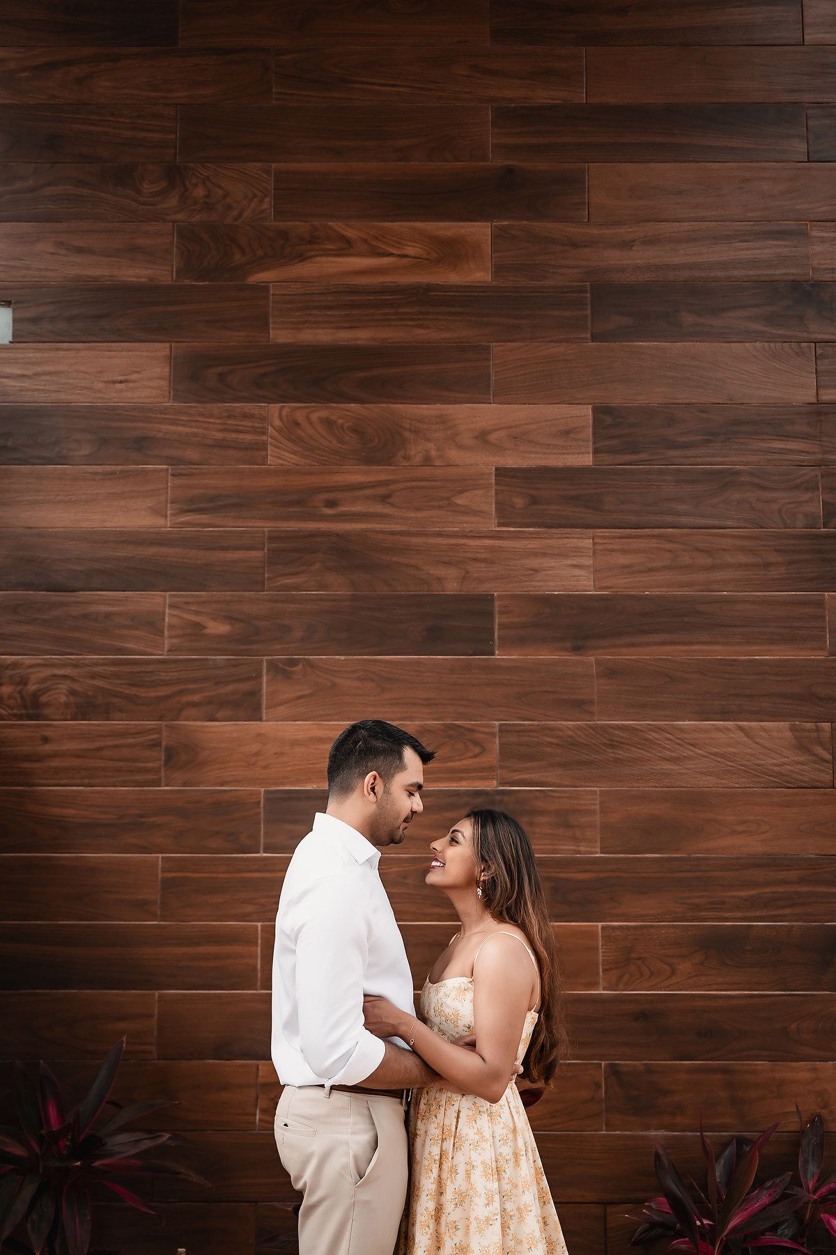 Romantic couple in white and peach outfits dancing against a wooden wall backdrop.