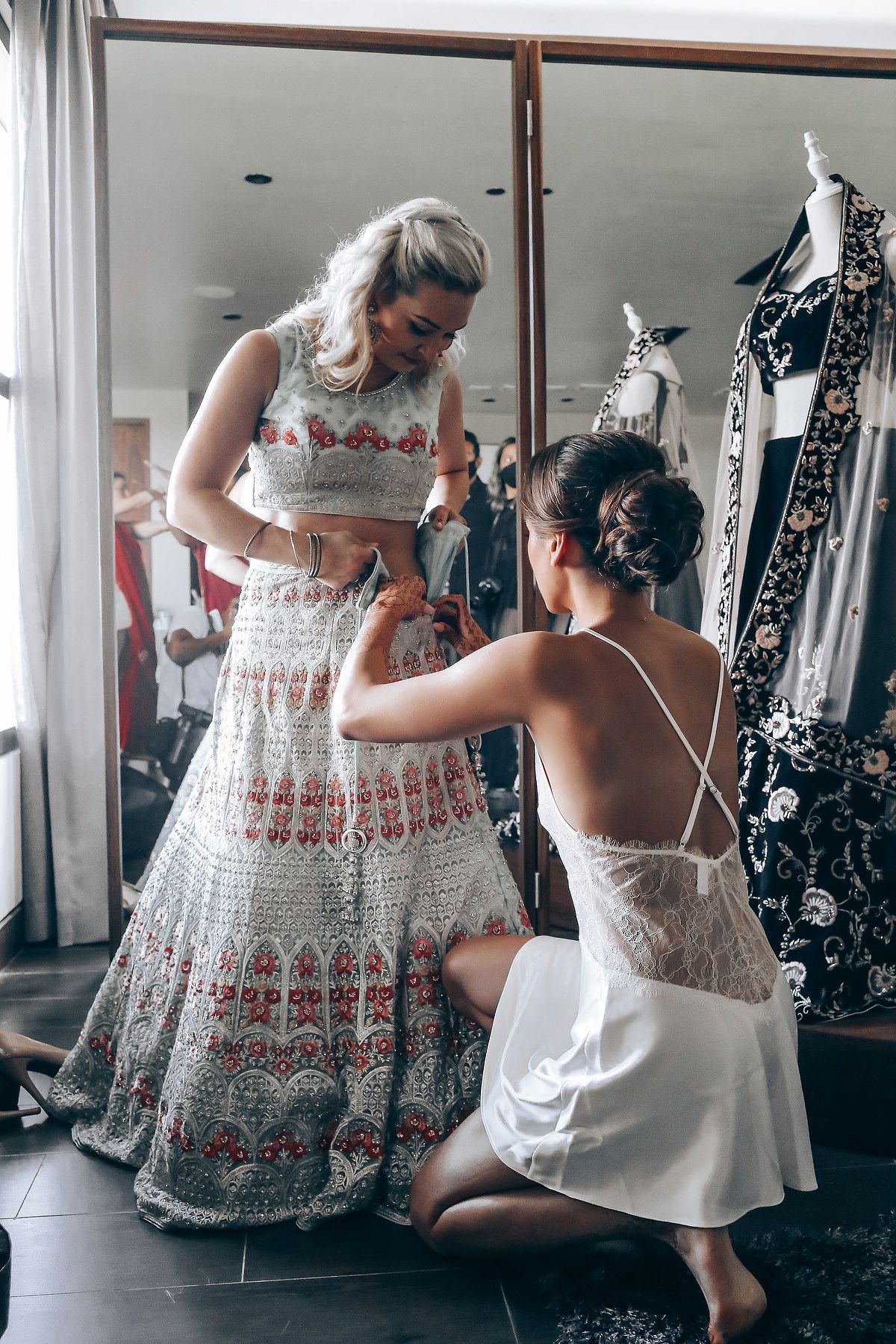 A series of photos showing someone helping another person get dressed in a white and red patterned dress.