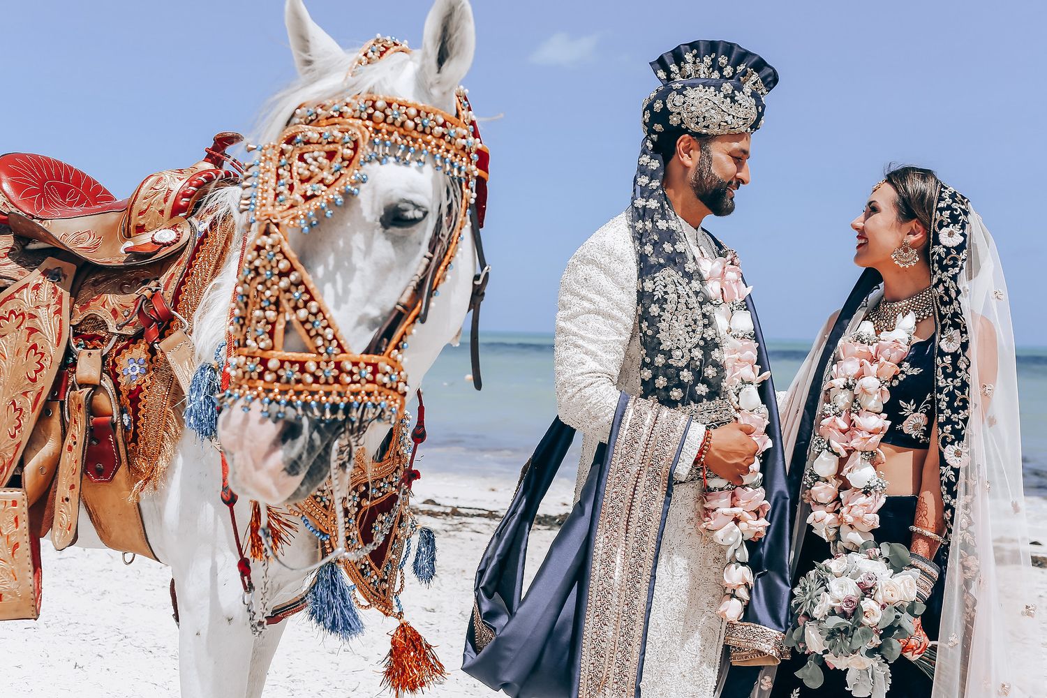 A wedding ceremony on a beach with the couple and guests wearing traditional Indonesian attire and accessories.