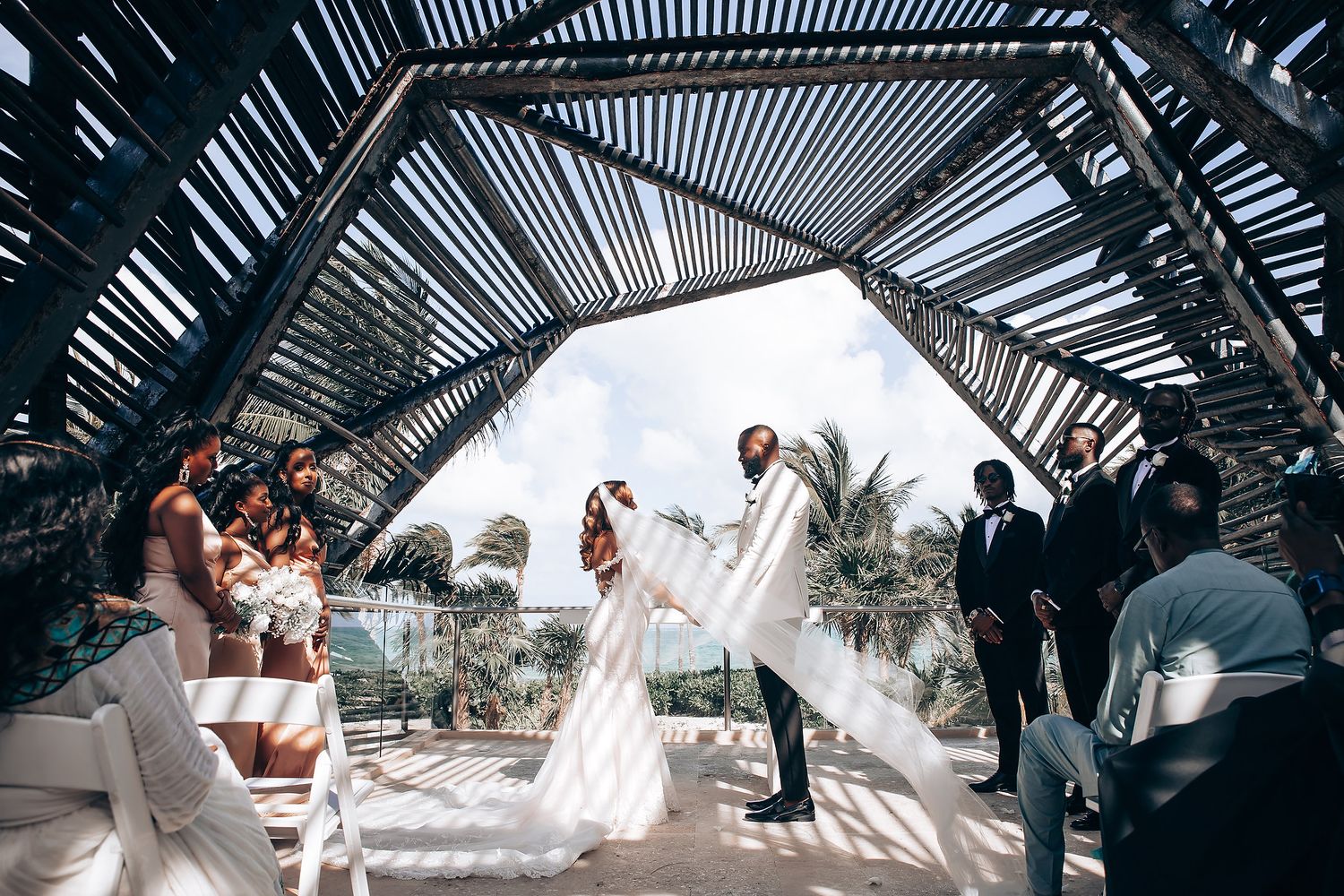 Wedding ceremony captured from ground level showing geometric shadows and palm trees.