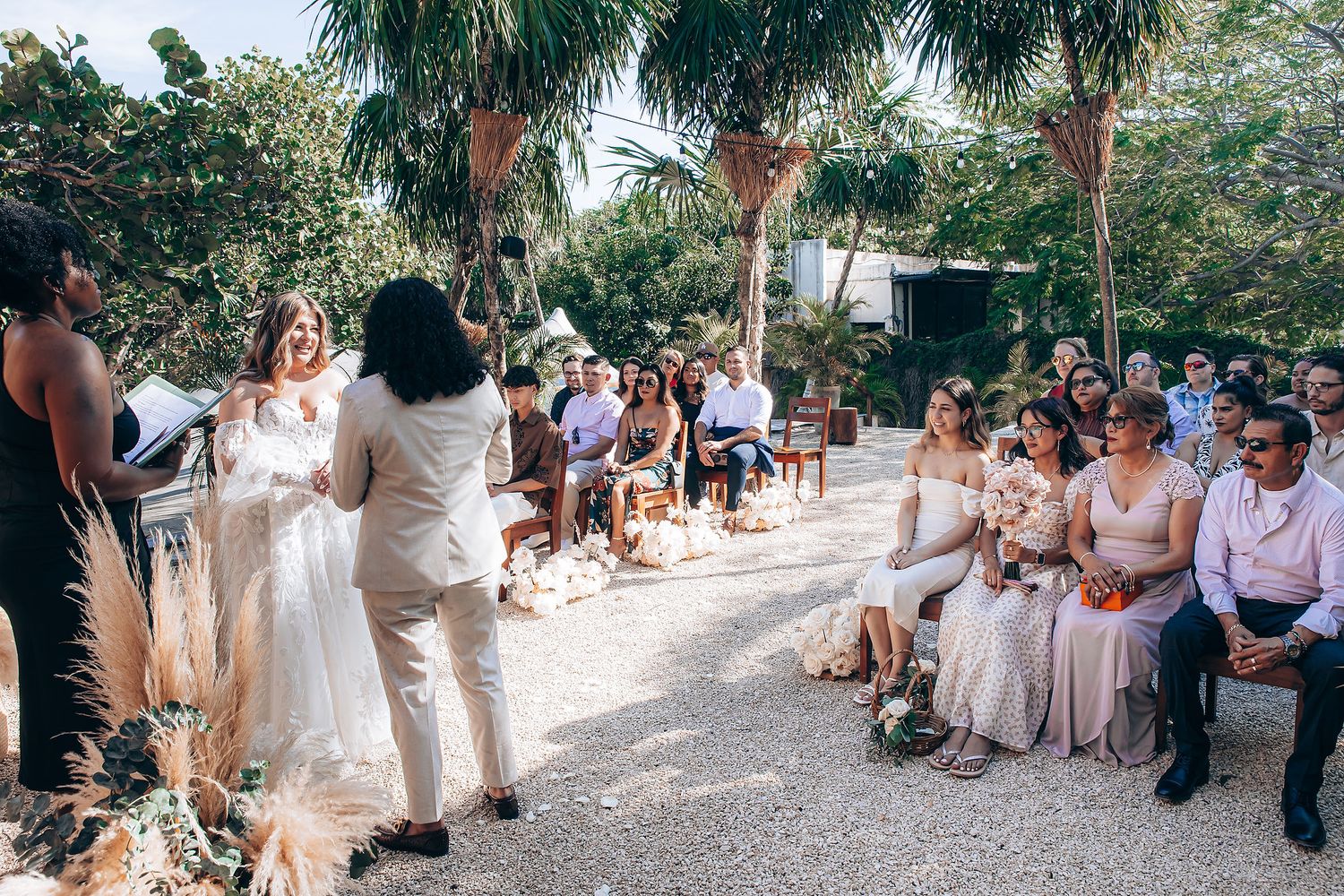 Wedding guests seated outdoors among tropical palm trees for the ceremony.