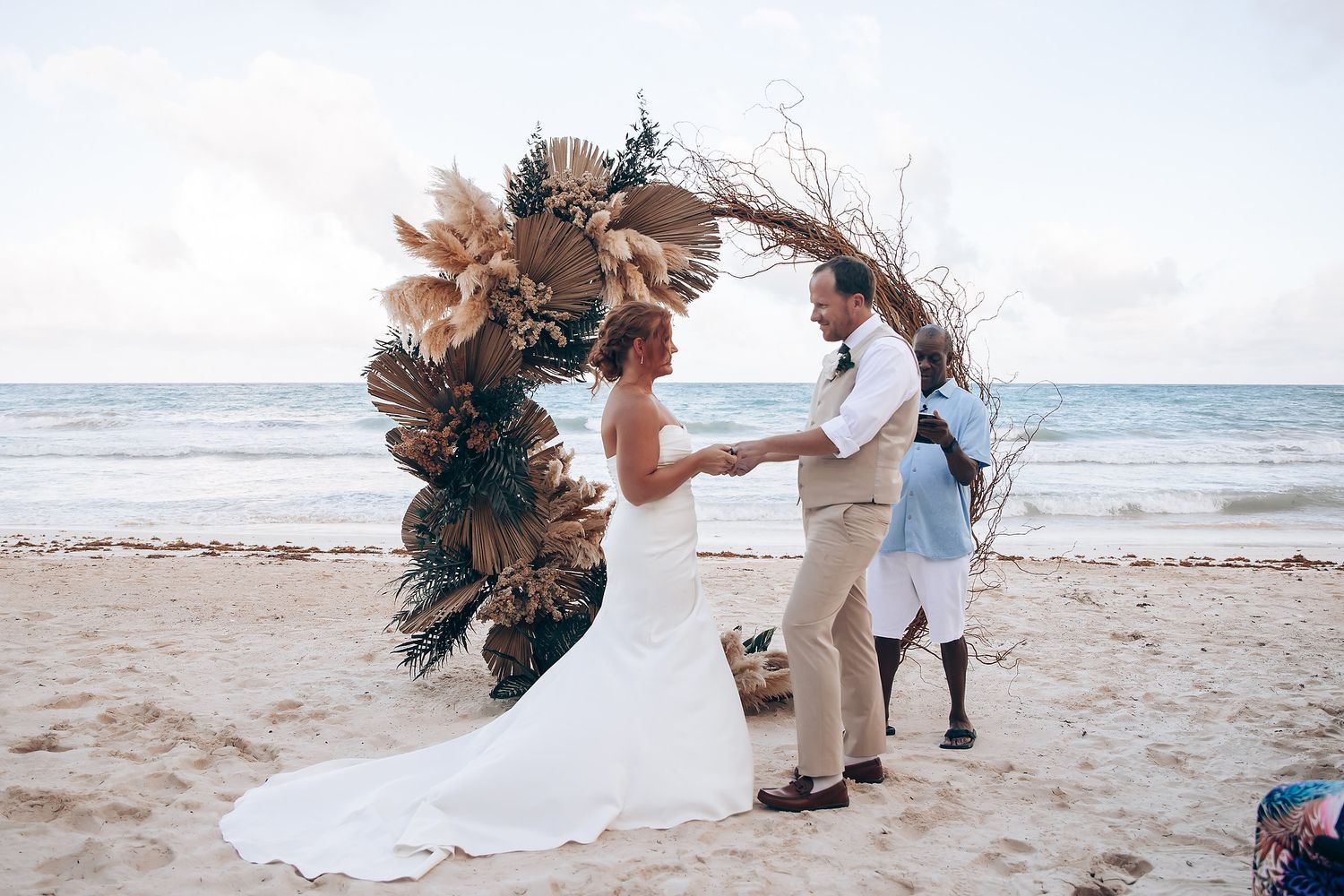 A romantic beach wedding ceremony setup with tropical floral arrangements and palm fronds on a sandy shore.