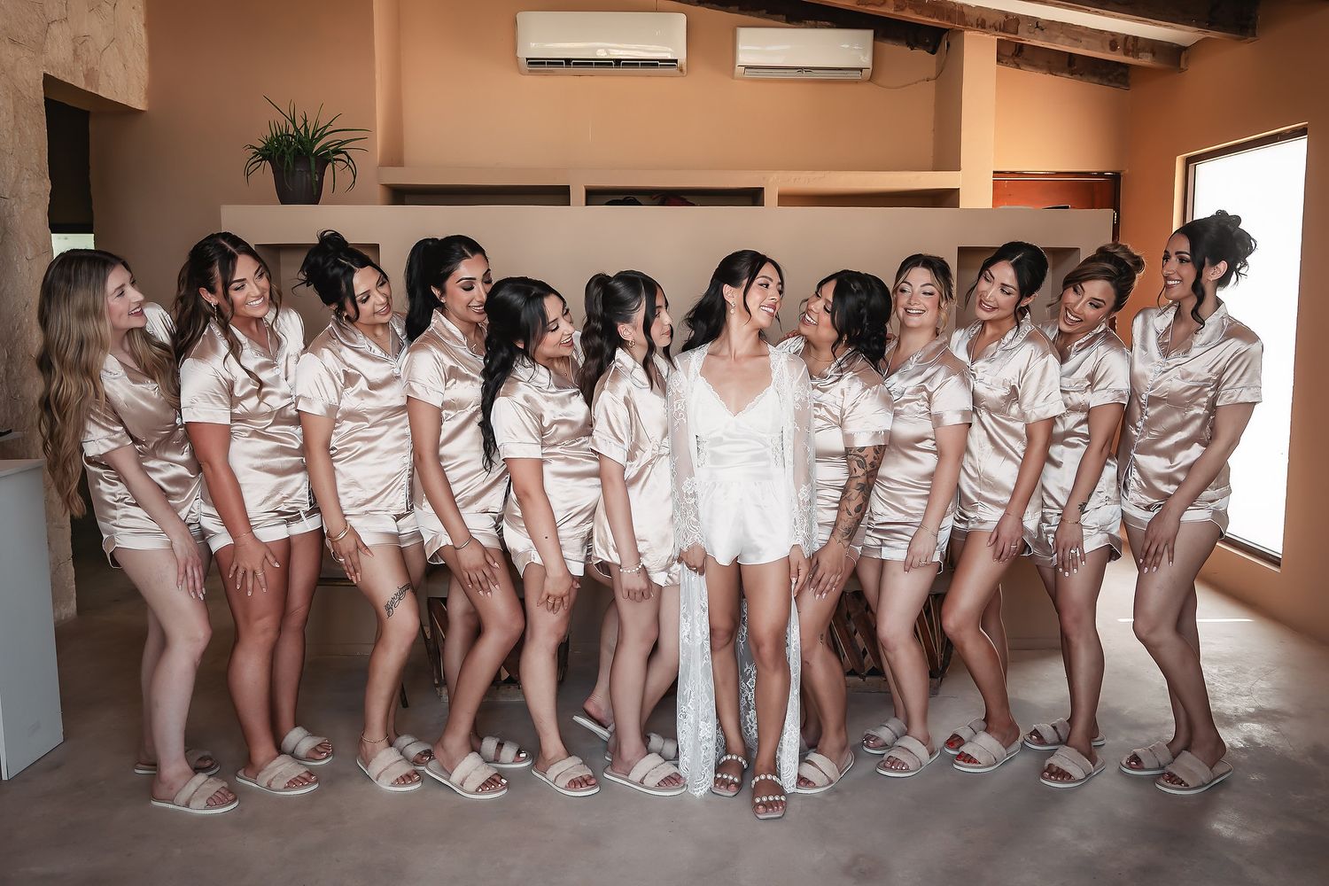 Large group of bridesmaids in matching silk robes posing together in an indoor venue.