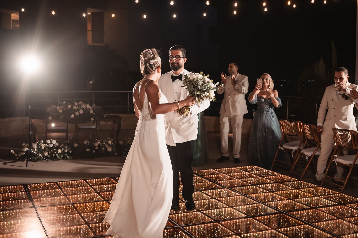 A romantic first dance moment captured on a glowing dance floor under string lights.