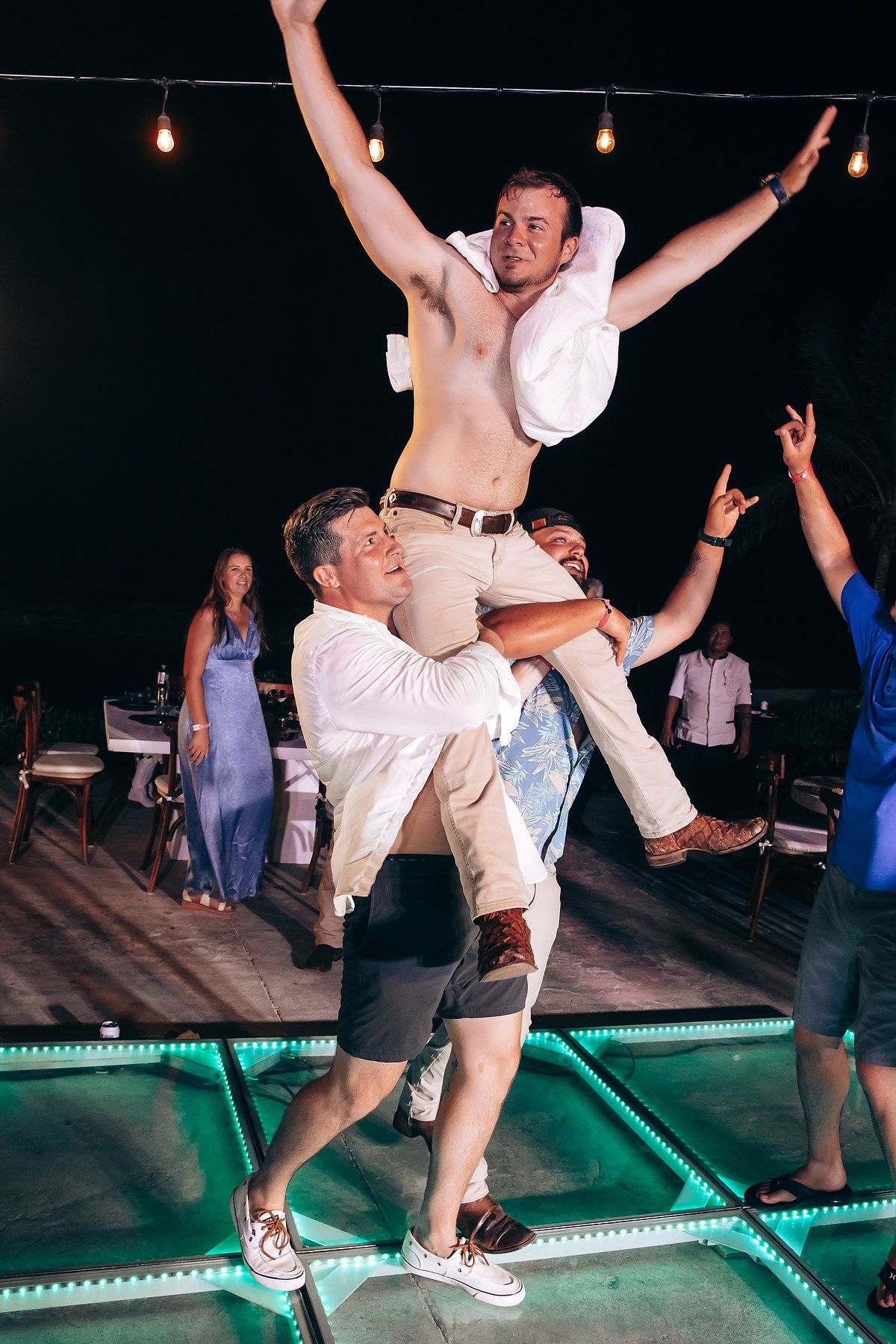 Energetic dance party on an illuminated floor during a wedding reception.