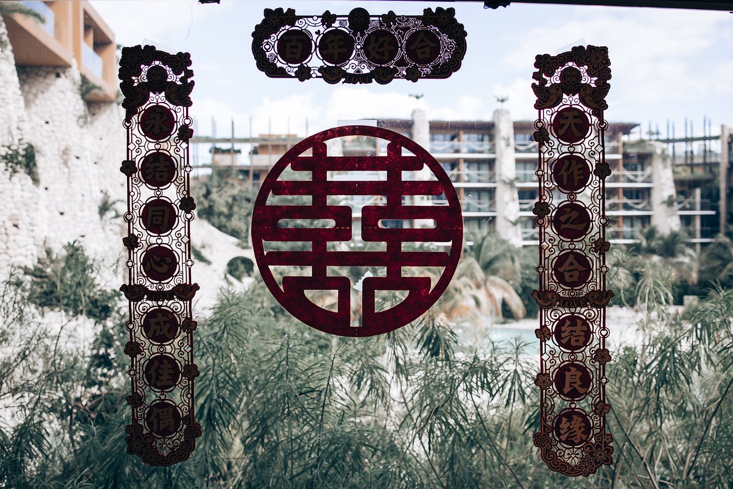 A traditional Chinese double happiness symbol and ornate patterns viewed through a window with urban buildings in background.