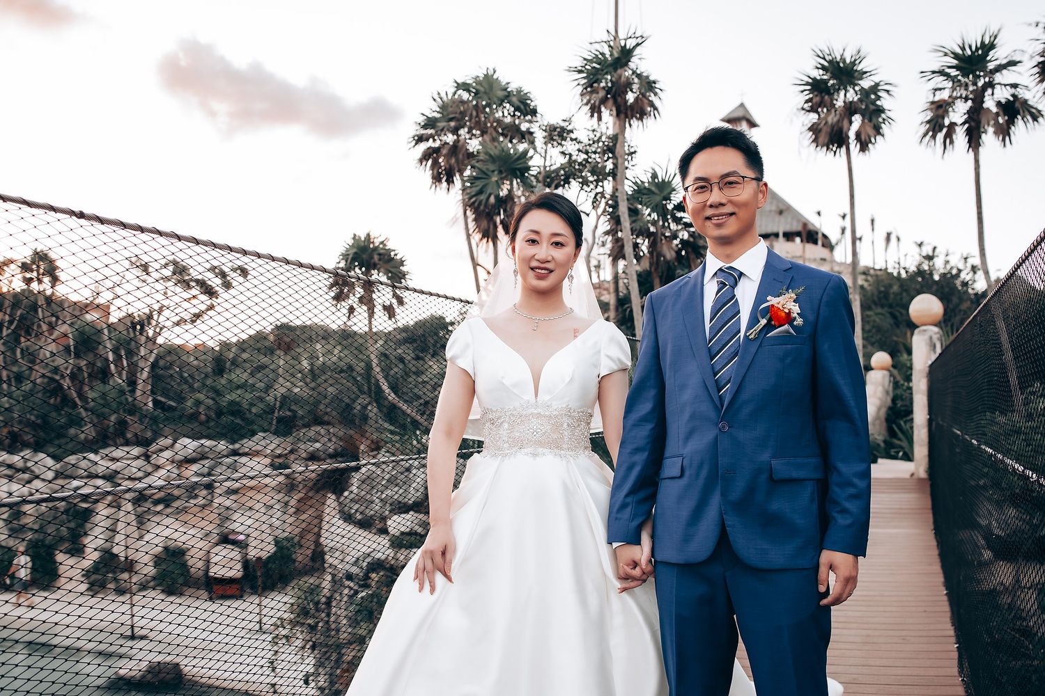 Outdoor wedding portraits with palm trees and stone architecture in the background.