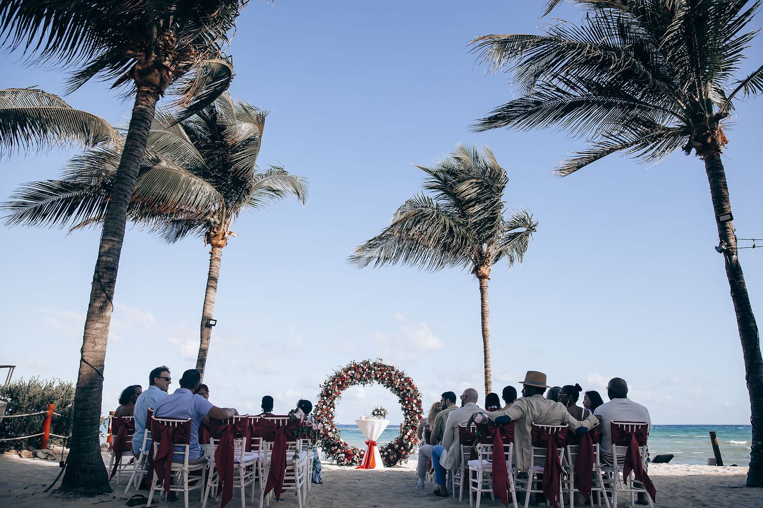 Wedding ceremony setup on a tropical beach with palm trees and an ocean view.