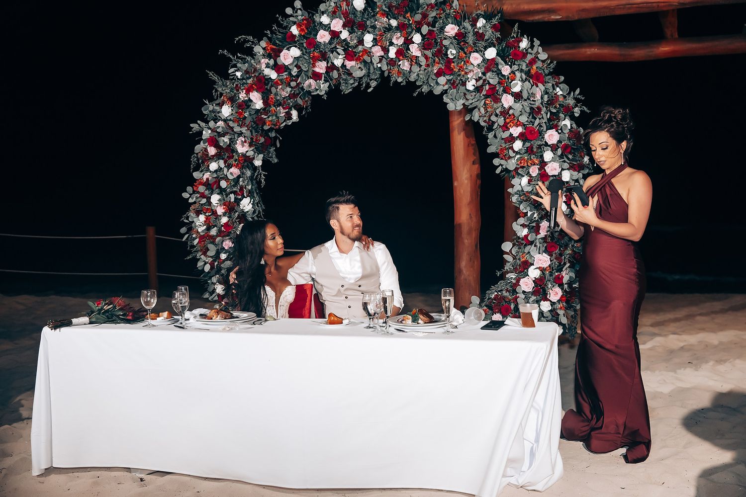 Wedding reception table decorated with red and white floral arrangements.