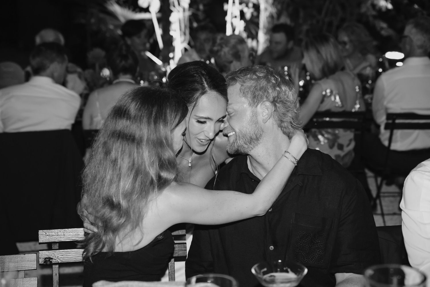 Black and white photo of three people sharing an intimate moment at an elegant evening event.