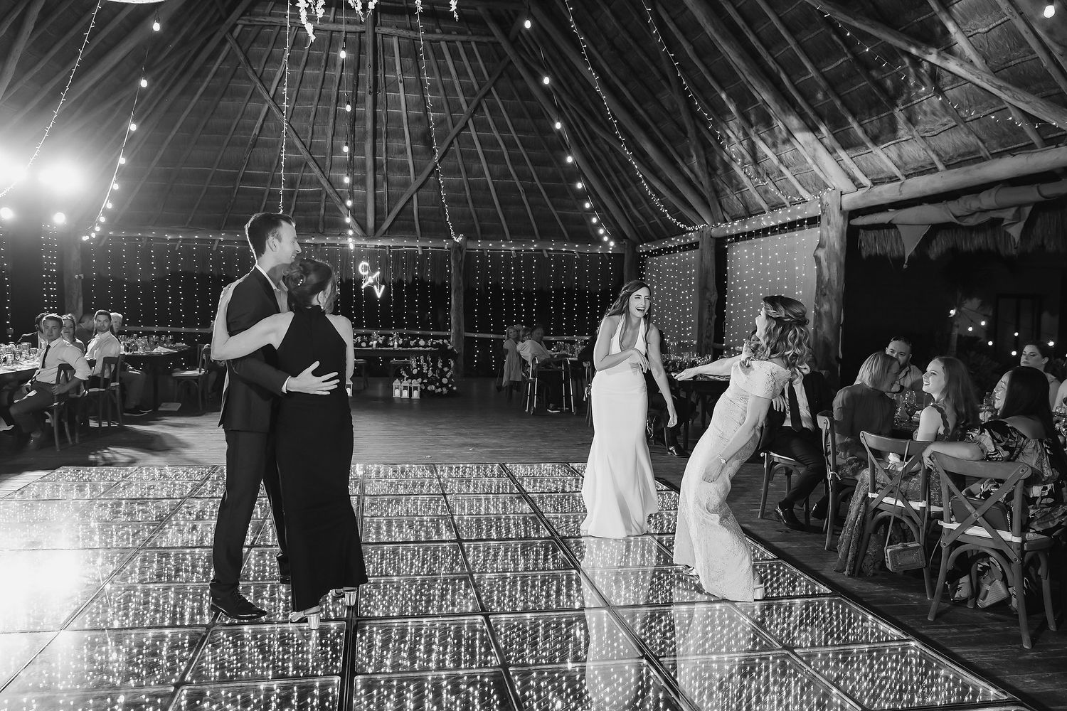 Black and white photo of bride and groom sharing first dance in elegant barn venue with string lights.