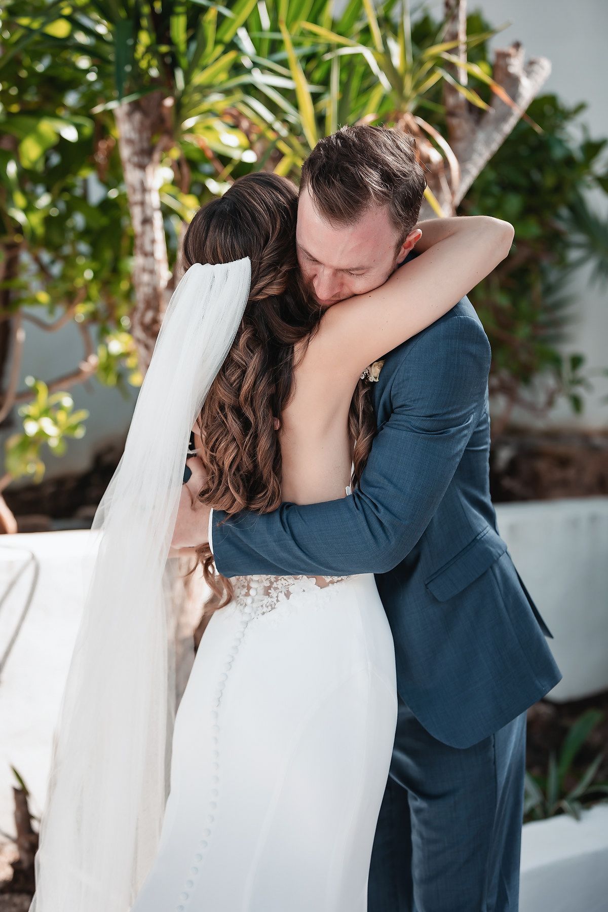 Bride and groom share an emotional first look hug outdoors, surrounded by tropical greenery at their wedding ceremony.