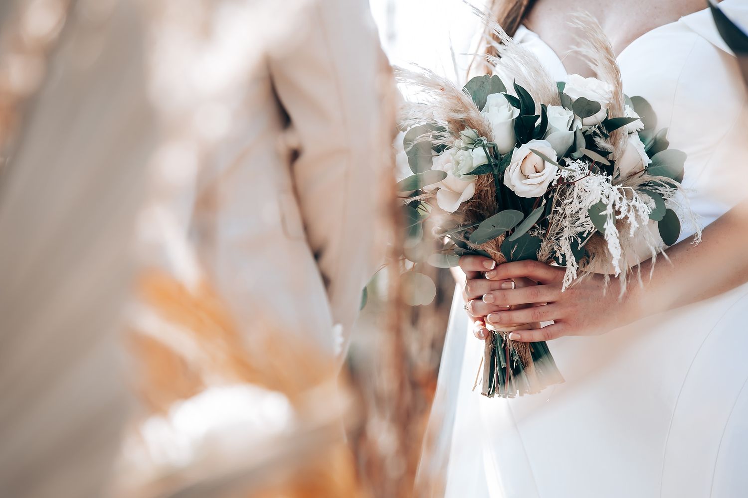 A delicate white bridal bouquet with roses and eucalyptus leaves held against a light background.