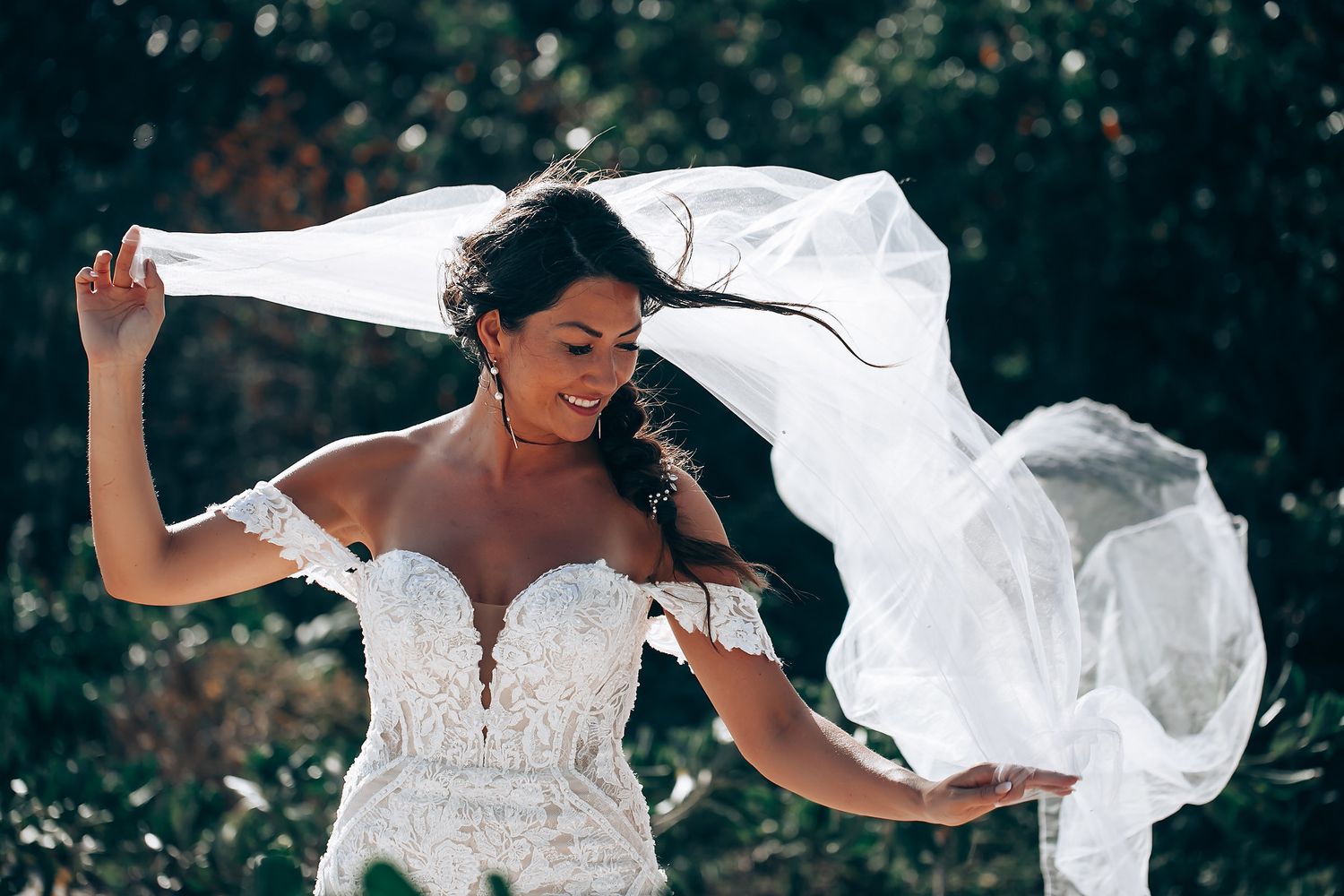 A white lace wedding dress billows dramatically in the tropical breeze.