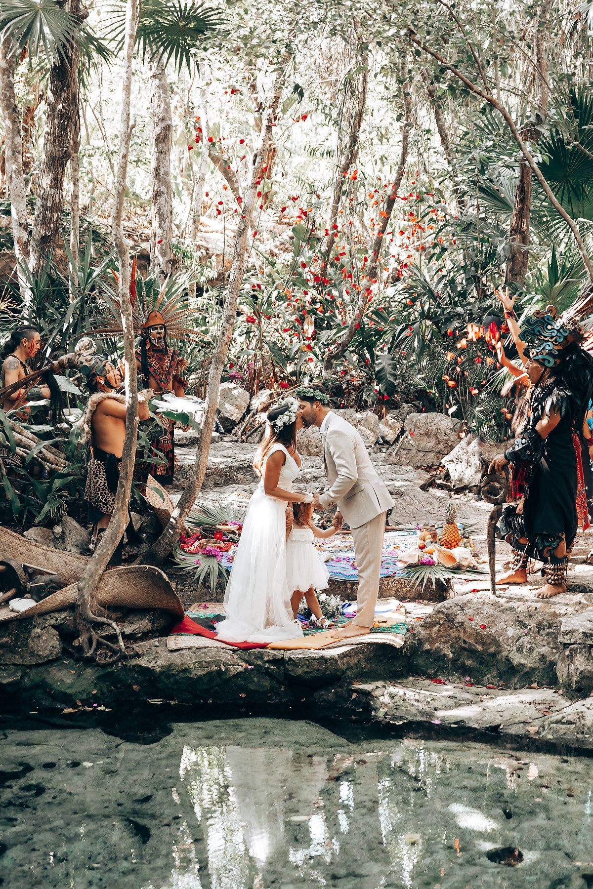 A wedding ceremony takes place beside a reflective cenote pool in a Mexican jungle setting.
