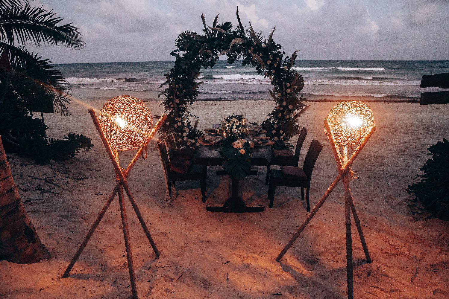 Beach wedding setup at sunset with tiki torches and ocean view.