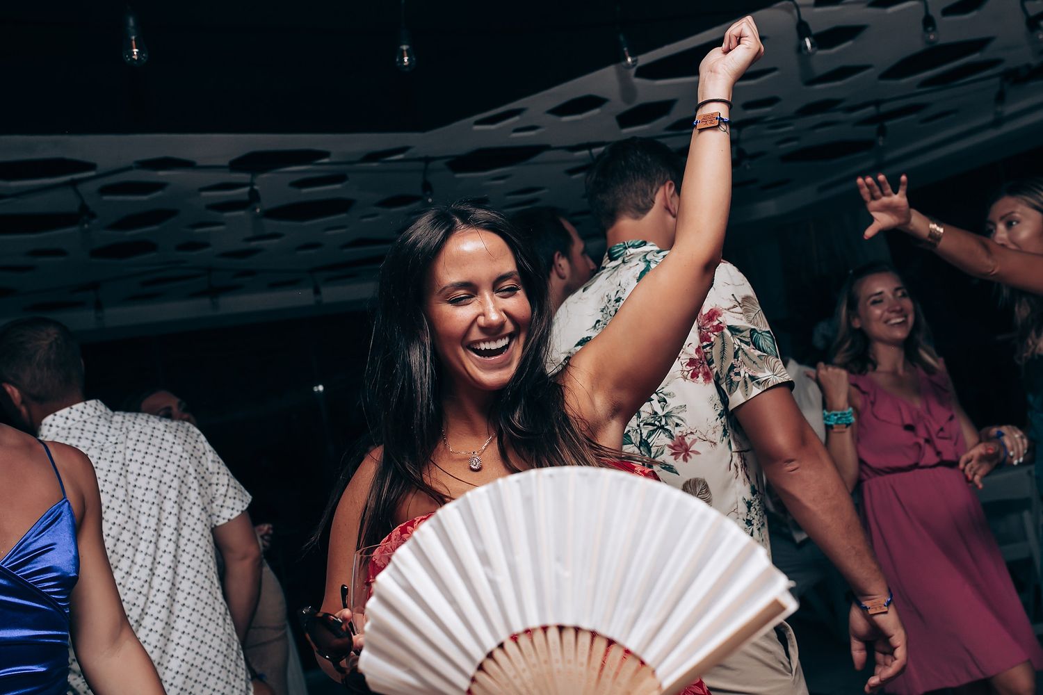 Wedding reception party guests dancing and celebrating with paper fans on the dance floor.
