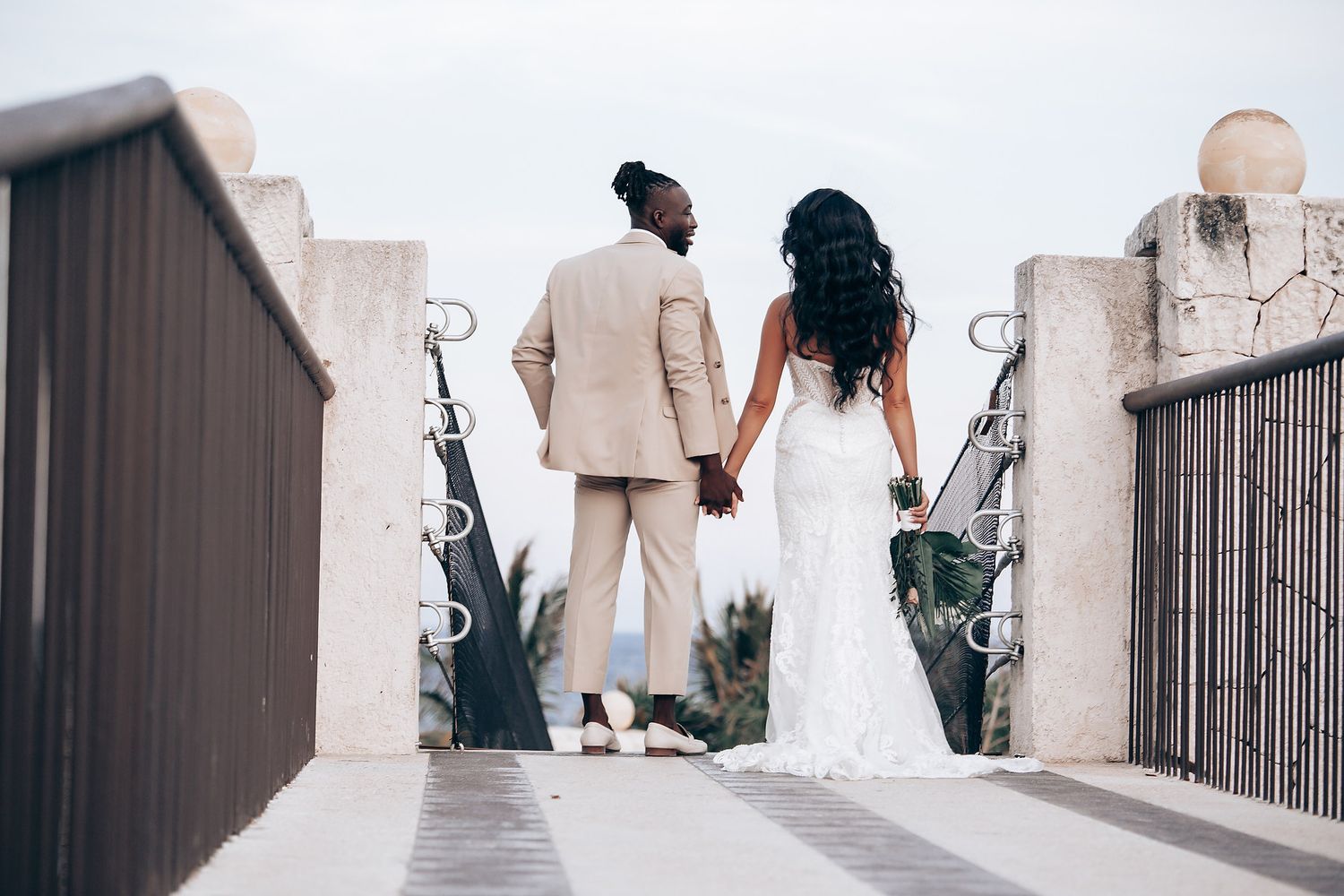 Elegant couple walking along a white stone pathway in wedding attire.