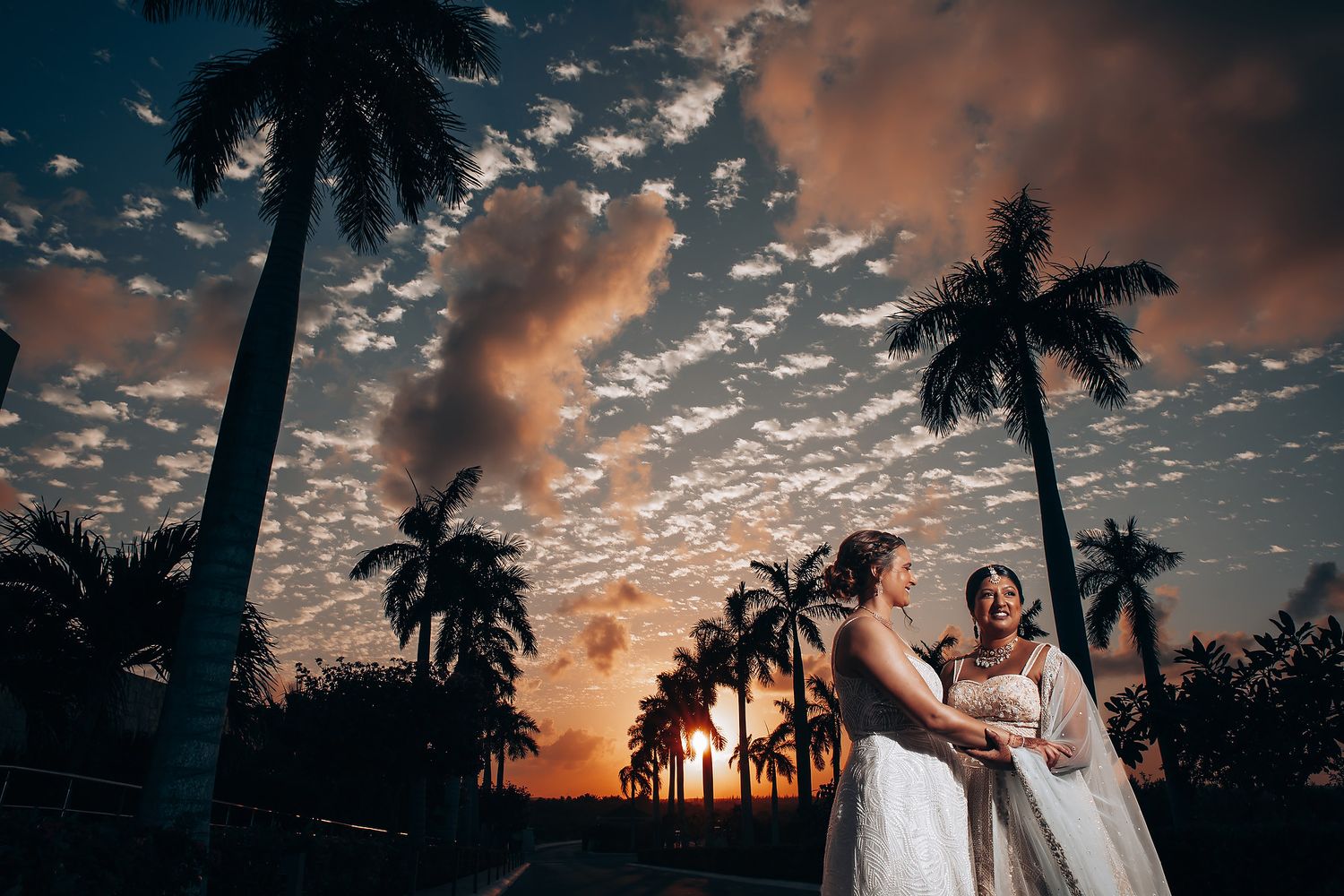 Romantic sunset silhouette with palm trees and dramatic orange sky at a beach wedding.