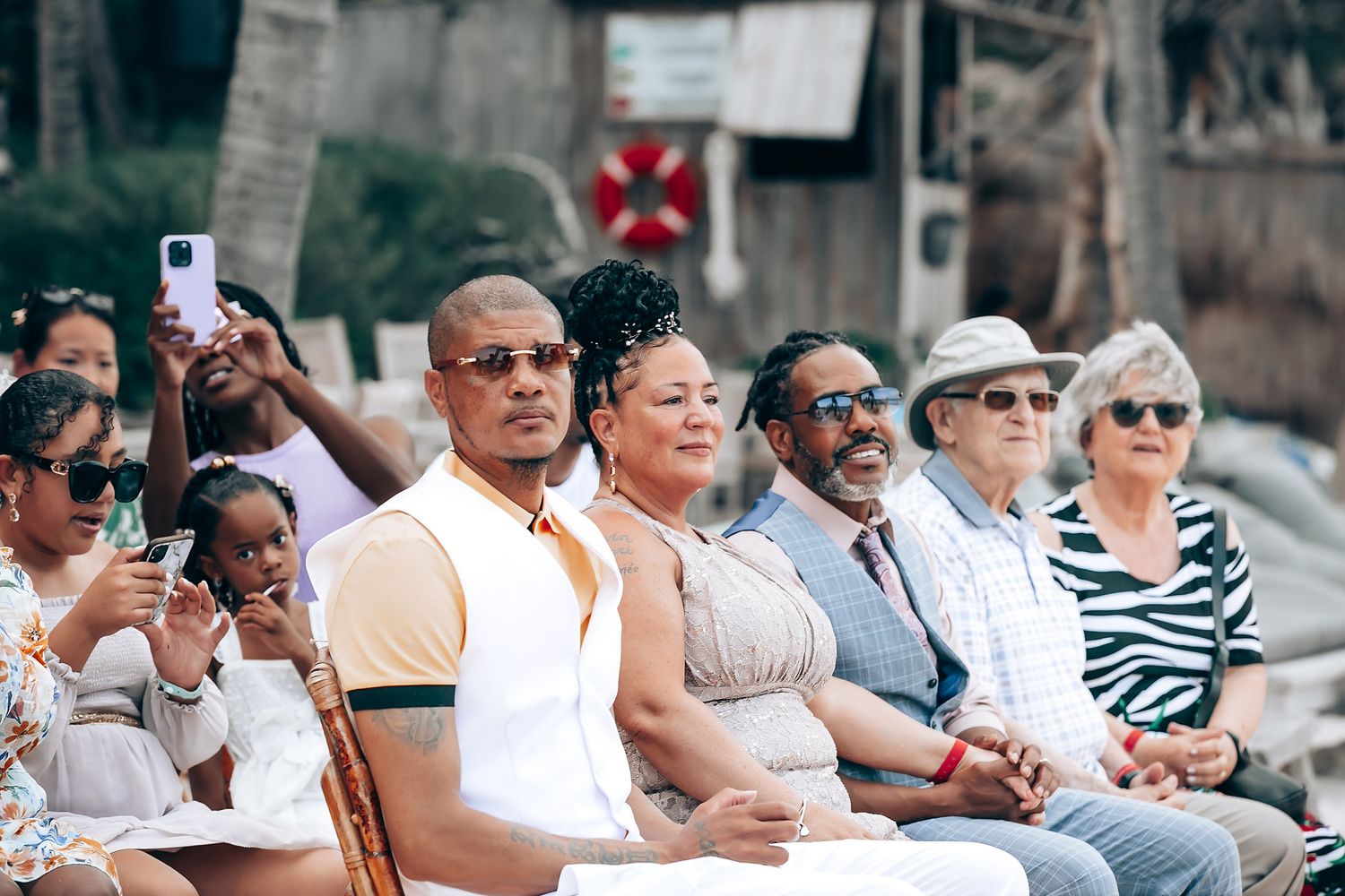 Wedding guests seated in white chairs watching a beachside ceremony.