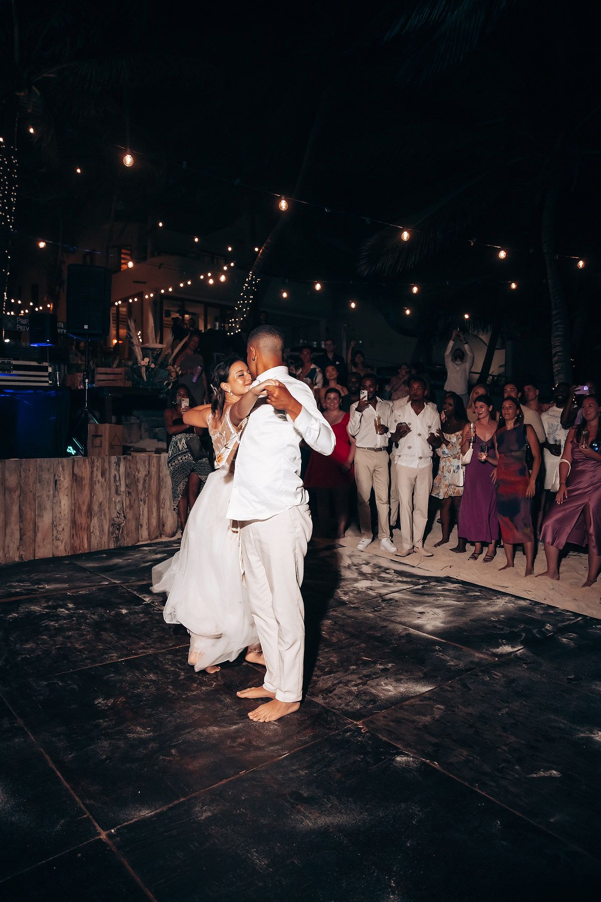 A wedding reception first dance under string lights on an outdoor dance floor.