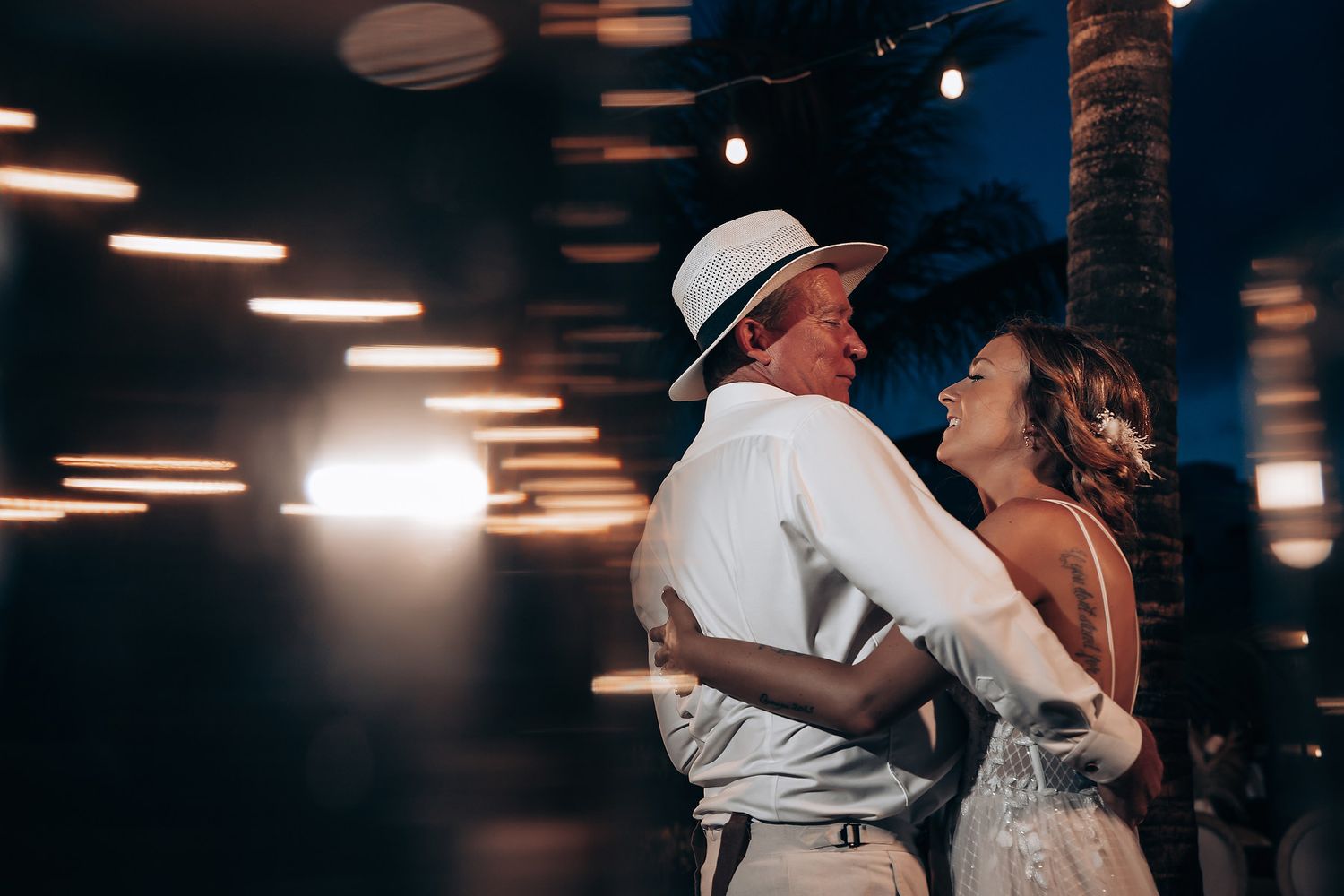 Wedding couple dances together during their evening reception with ambient lighting overhead.