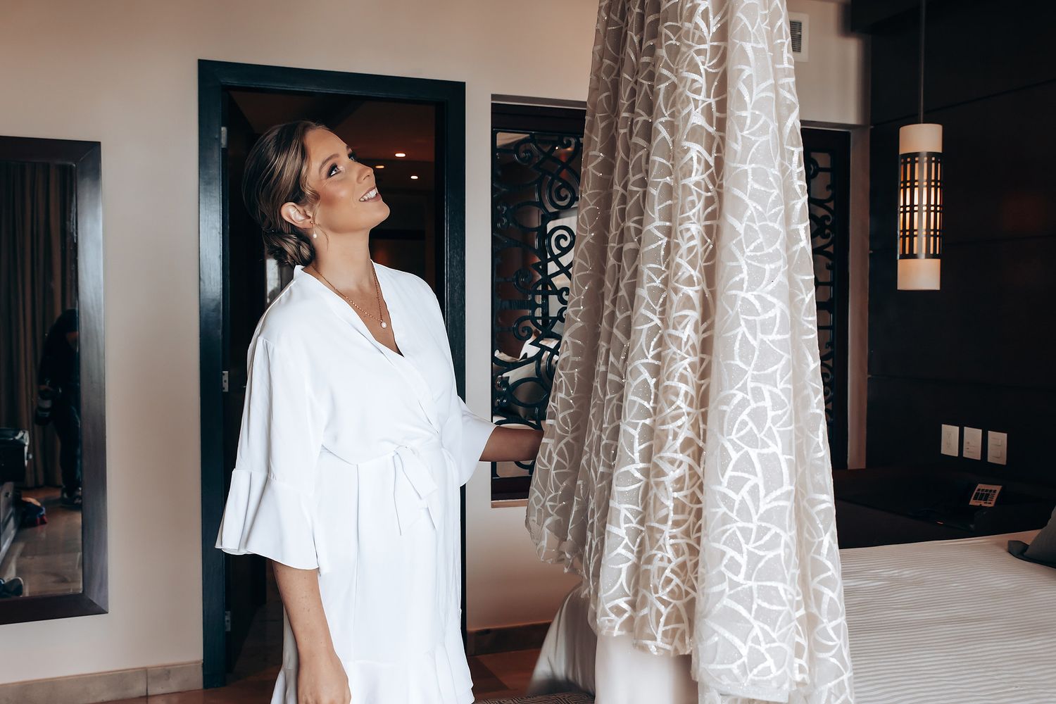 A woman in a white dress stands in a room with large windows.