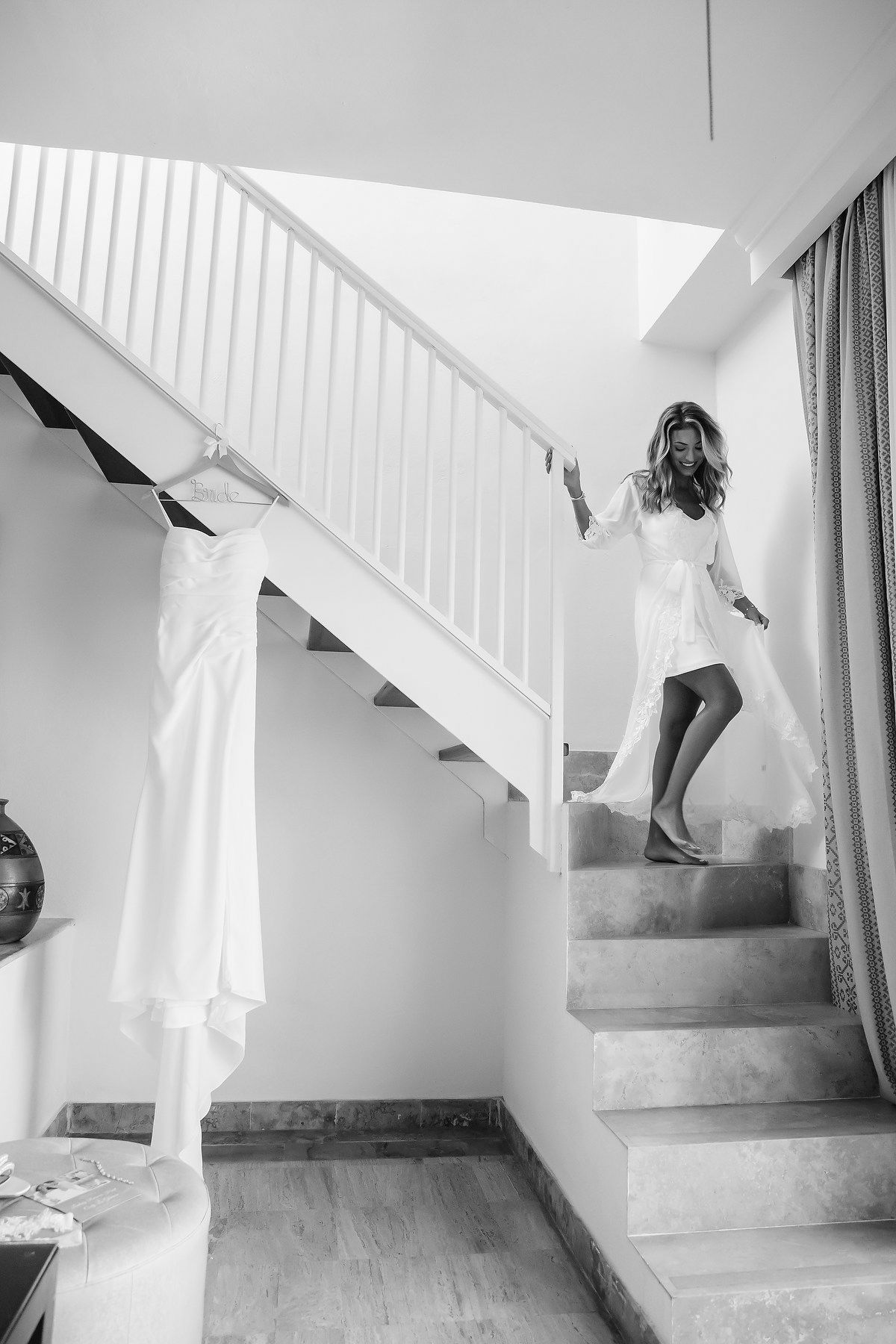 A woman in a white dress walks up a staircase in a bright, minimalist interior.