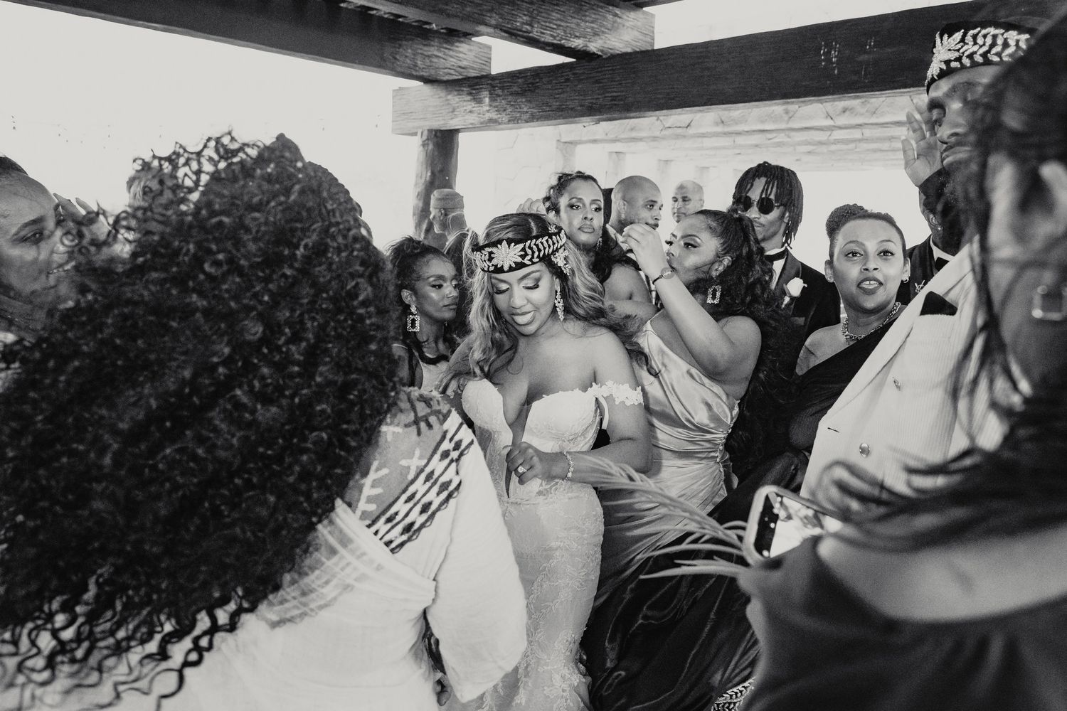 Black and white photo of lively wedding celebration with bride in Egyptian-inspired crown and white gown.