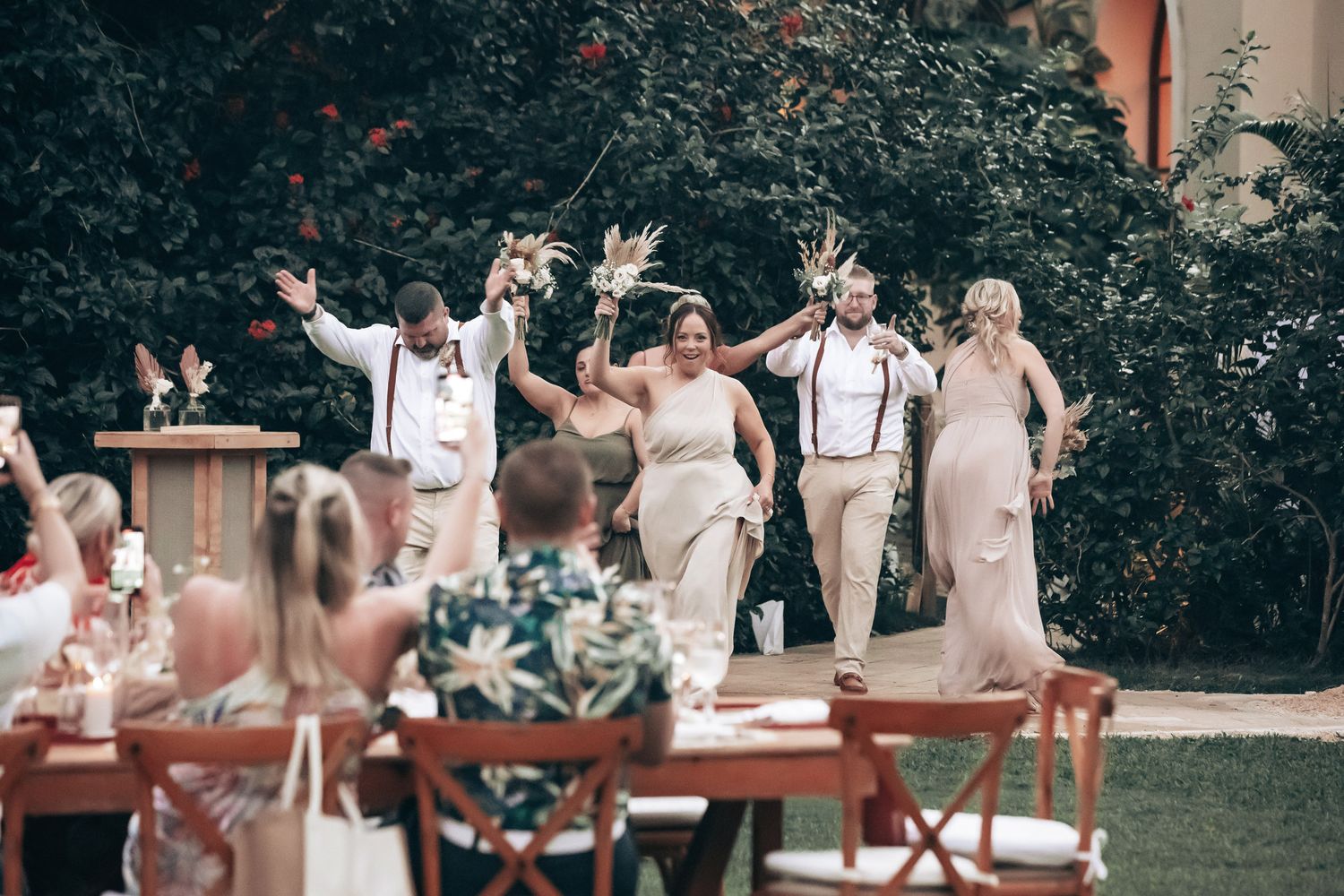 Wedding party makes a joyful entrance at an outdoor garden reception celebration.