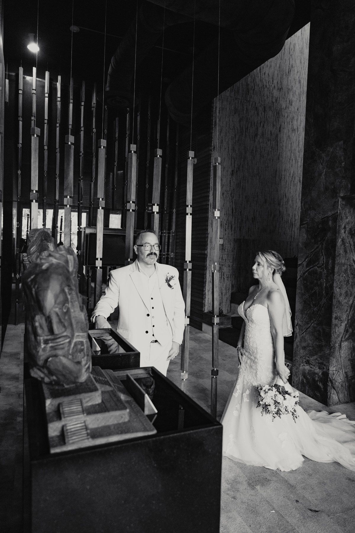 Black and white portrait of bride and groom in dramatic interior with sculptural decor.