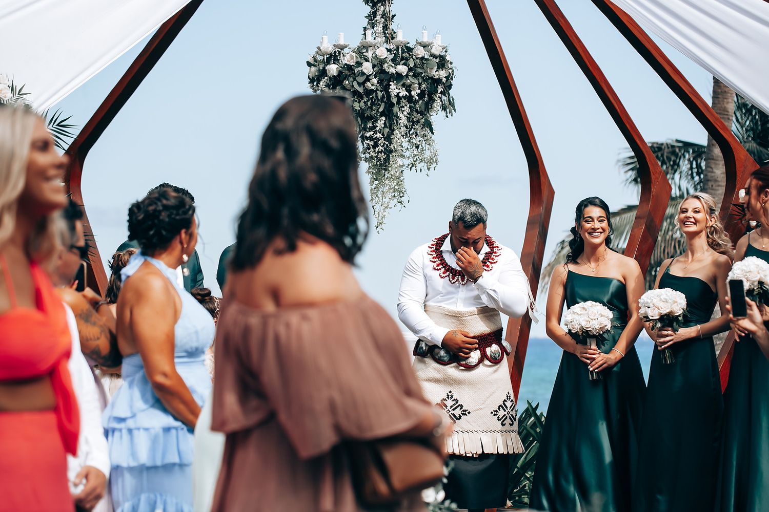 Wedding guests gather under a white canopy structure during an outdoor ceremony.